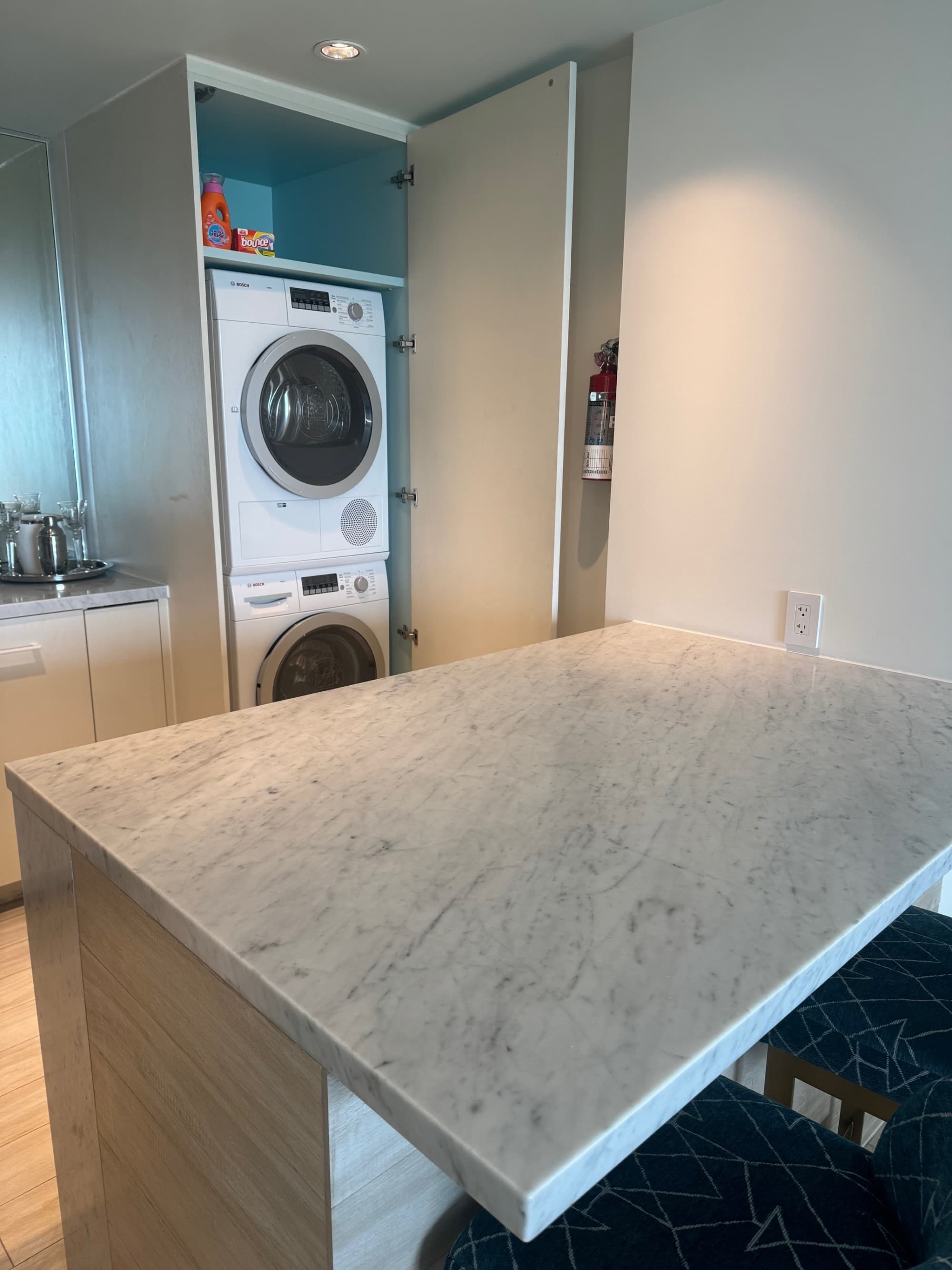 An image of a hotel suite with a stone countertop, washer and dryer cabinet and blank walls.