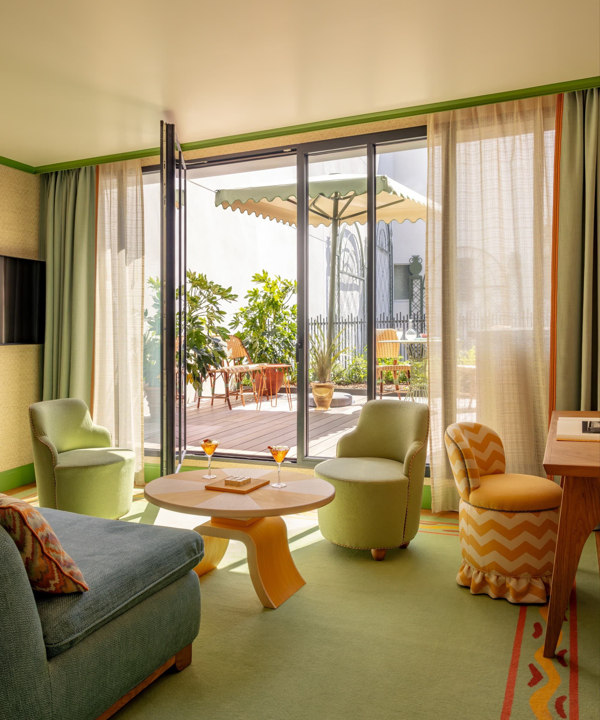 a luxe, colorful living room with a green carpet and blue and orange furniture overlooks a sunny terrace