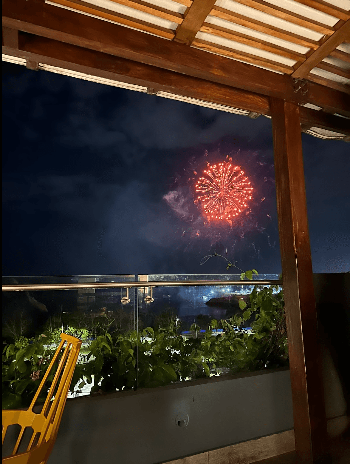 A picture of a red firework in the sky. There is a wooden pergola, bushes and a yellow basket in the forefront of the image.