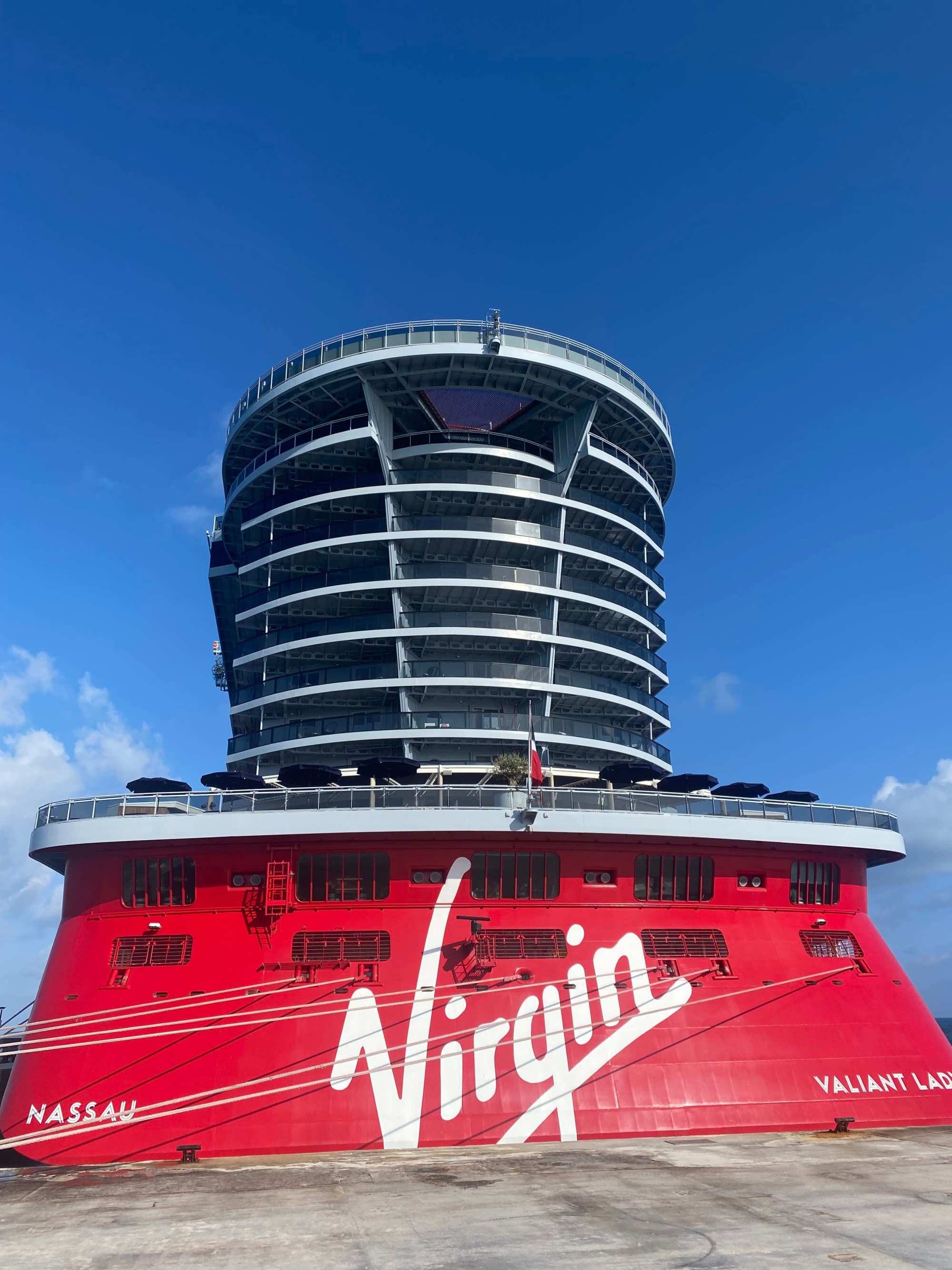 A view of the top of the cruise ship with a round set of balconies and a red painted exterior that reads "Virgin" in white lettering.