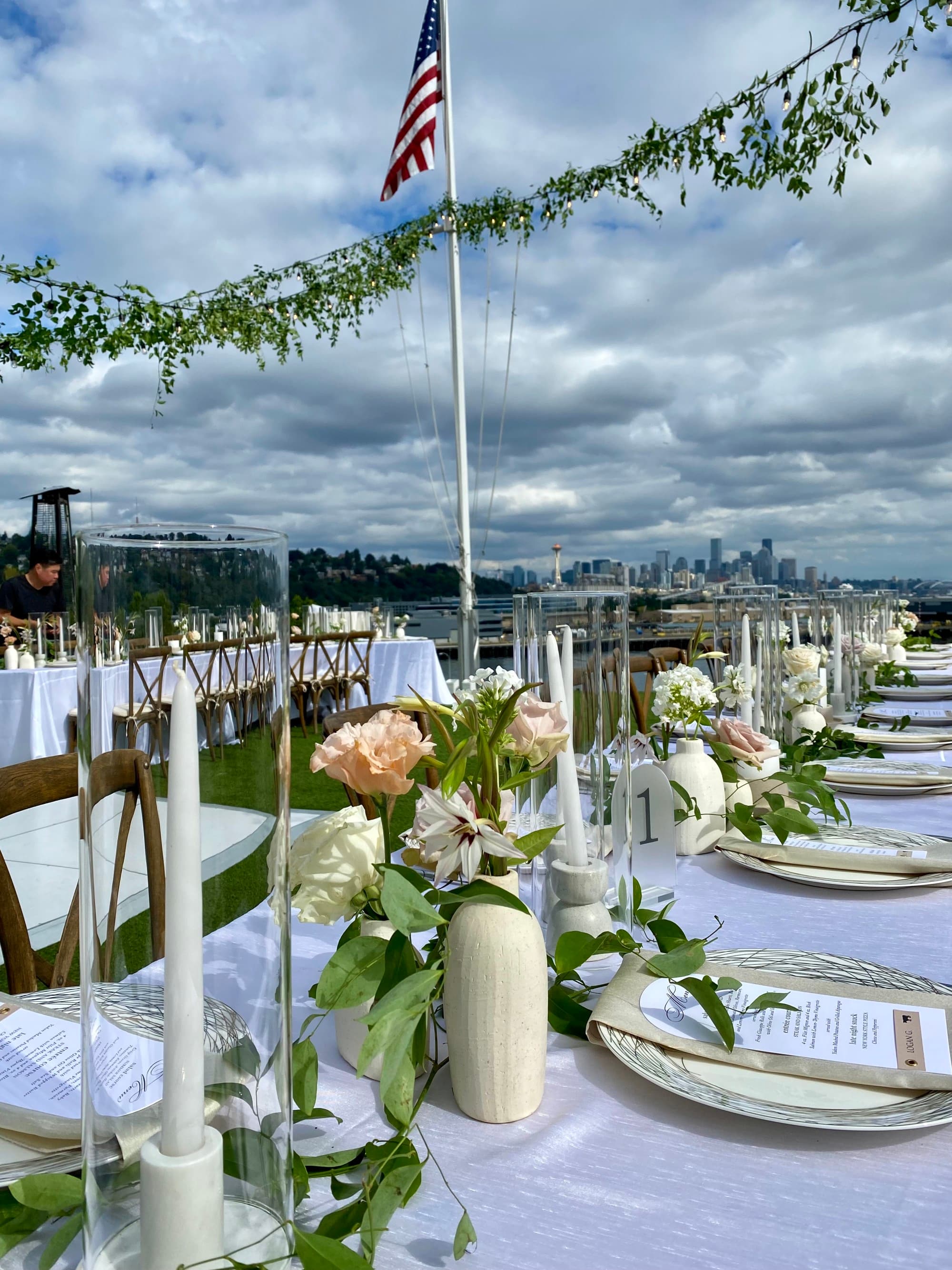 A wedding table with floral arrangements on the centerpiece, place settings, vines and an American flag in the background.