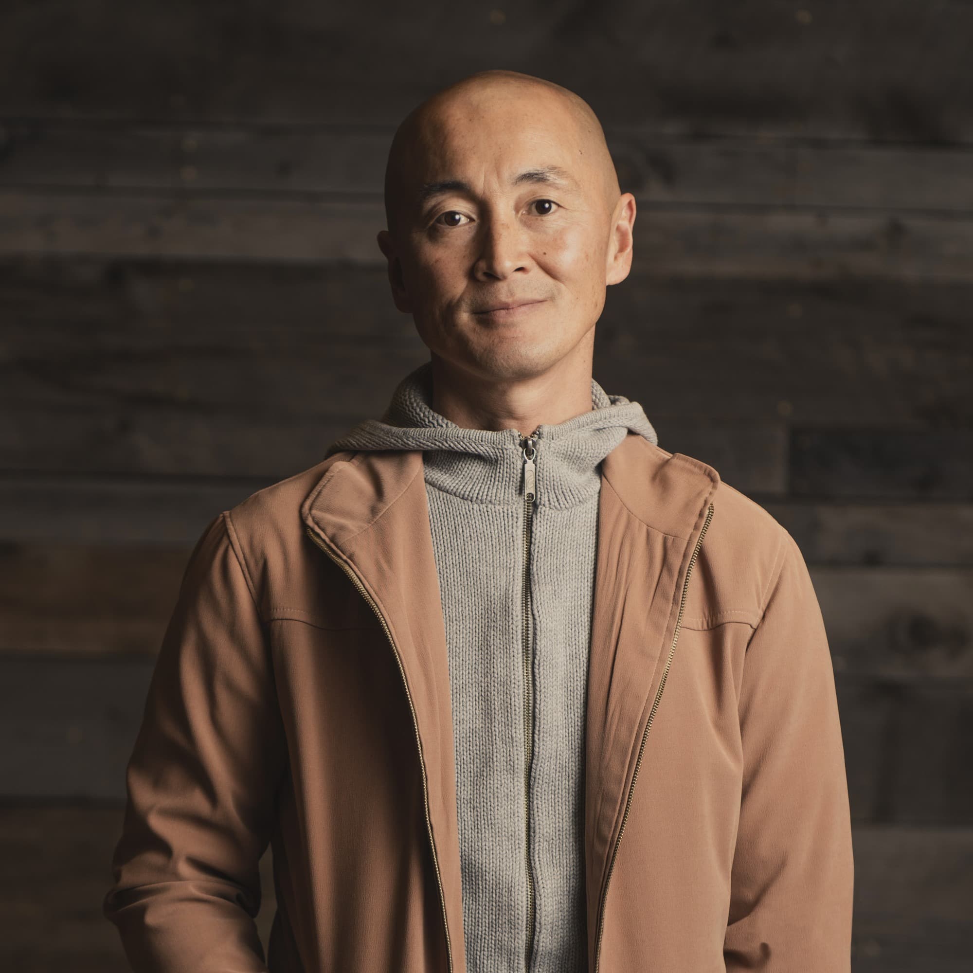 a bald man in a zip-up jacket and a gray shirt smiles