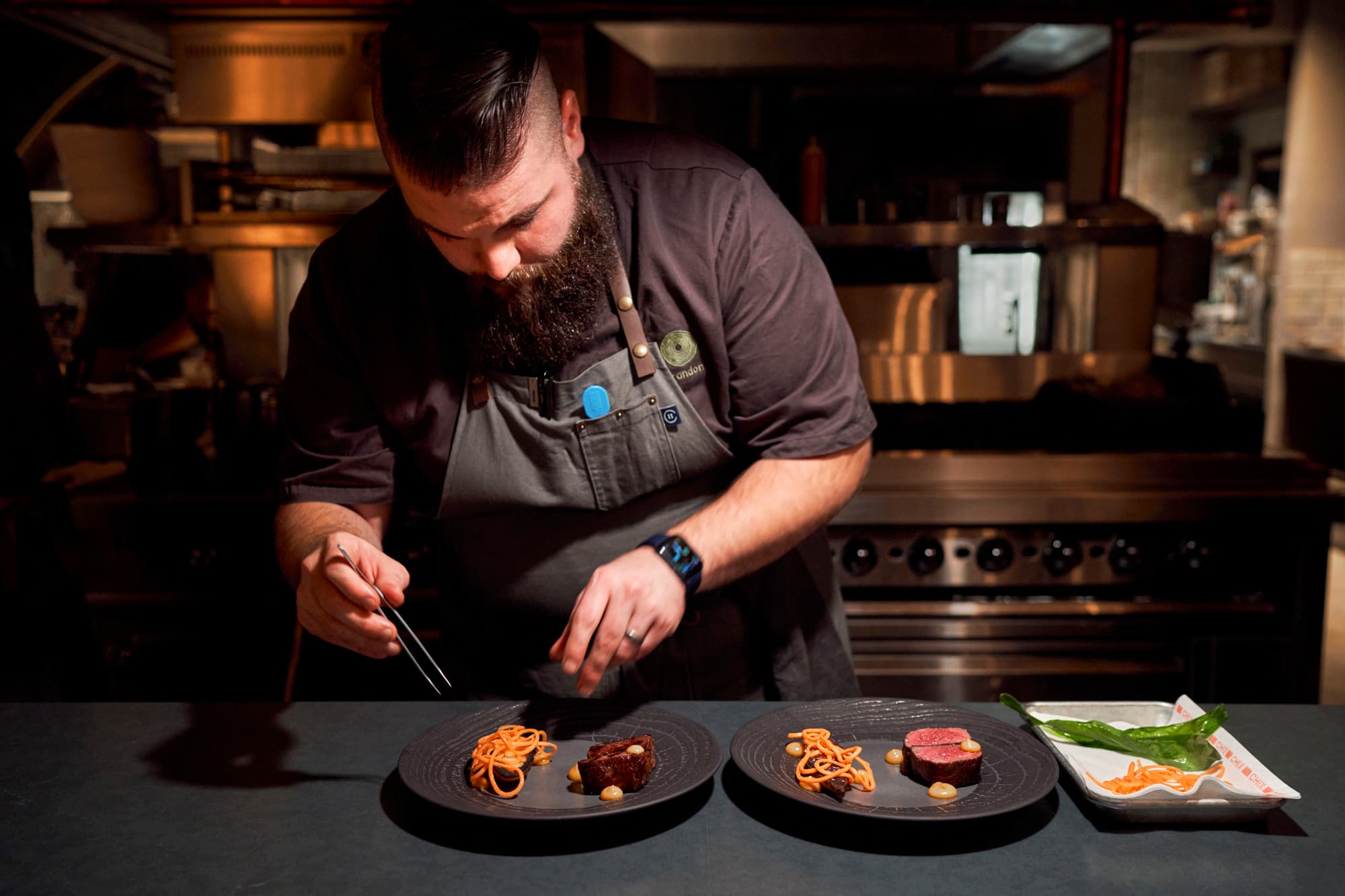 a man plates a fancy meal on a circular black plate