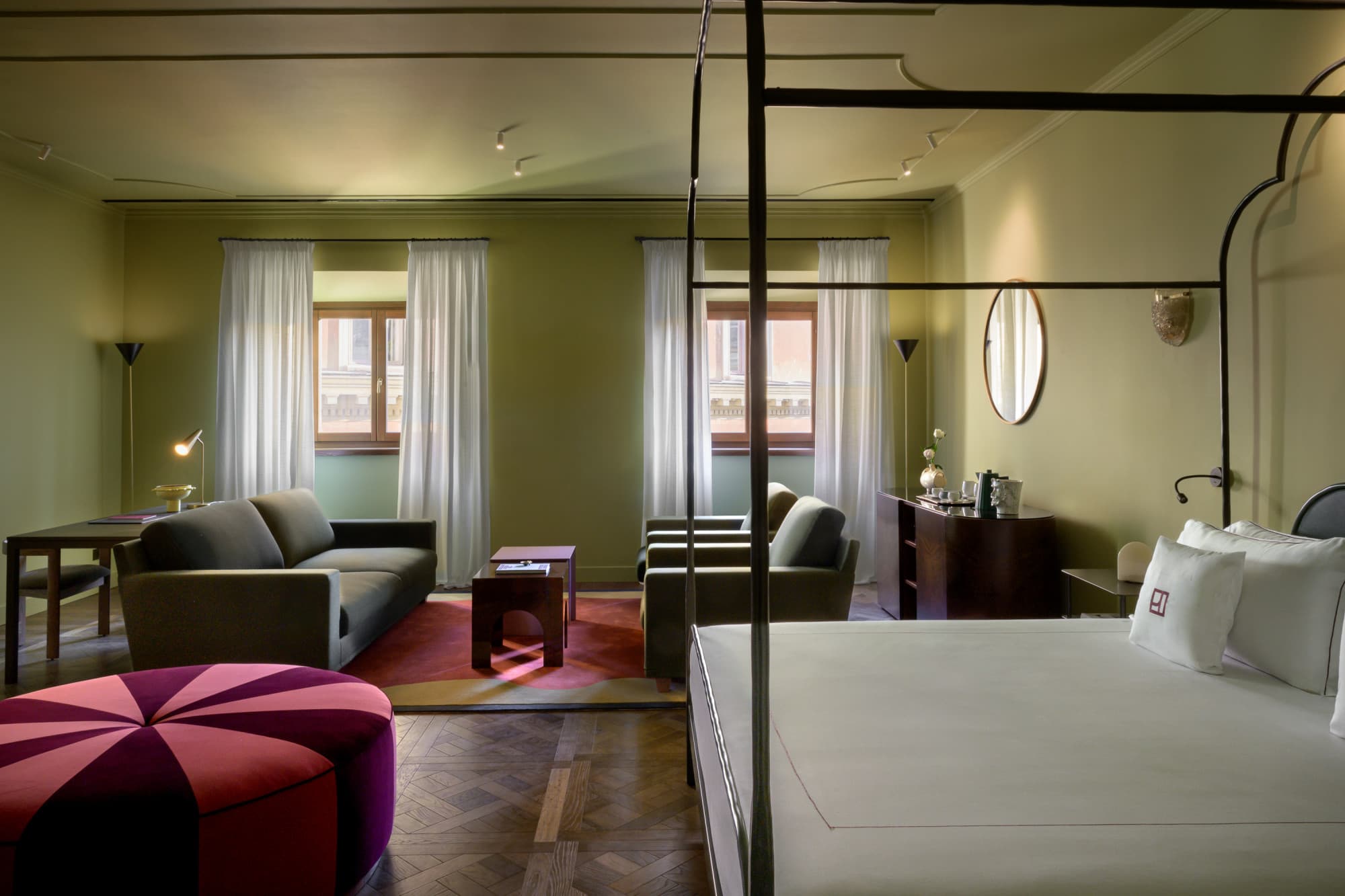a sprawling hotel bedroom with wooden floors and a burgundy pouf