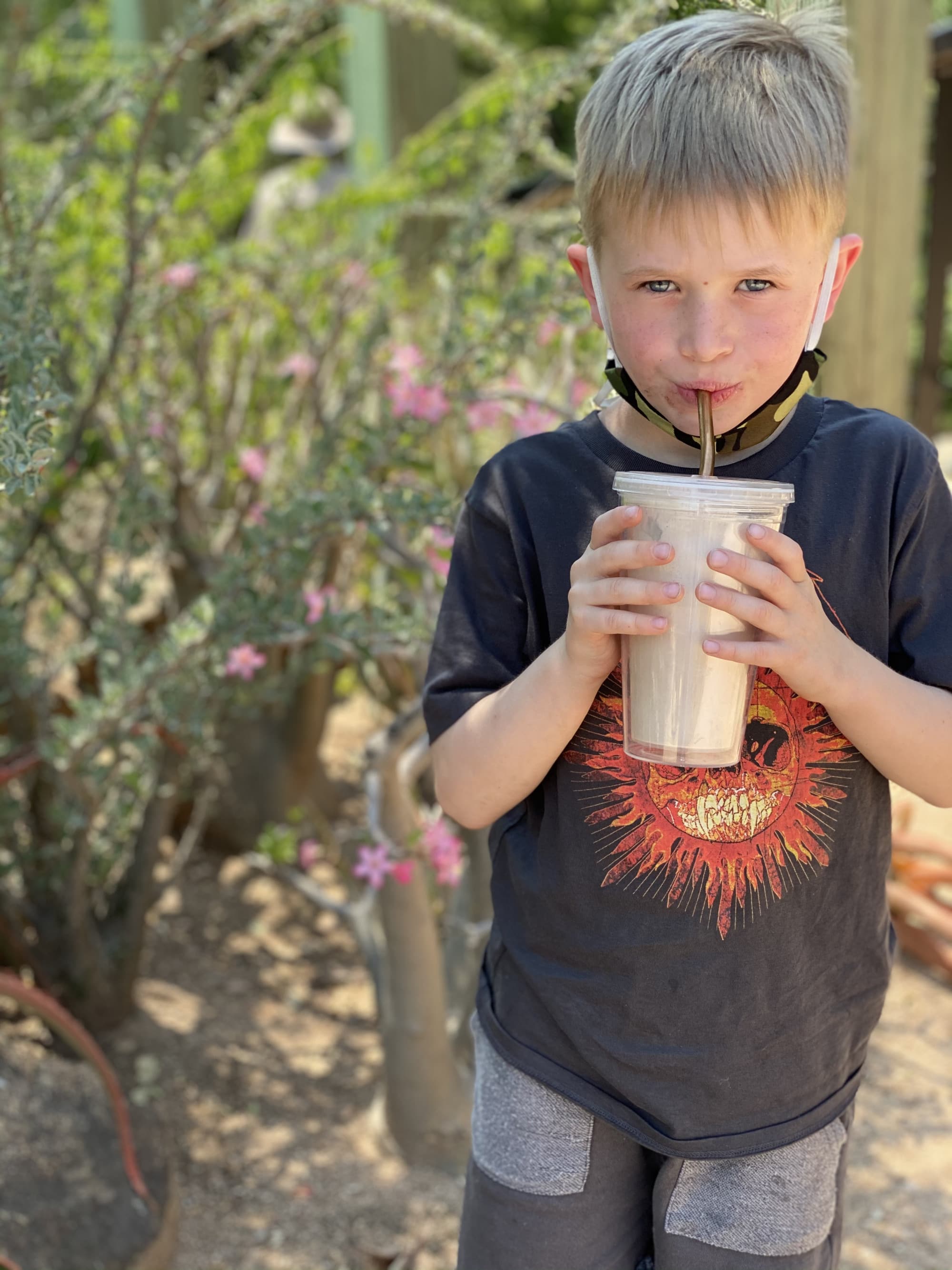 Child standing outdoors drinking a milkshake