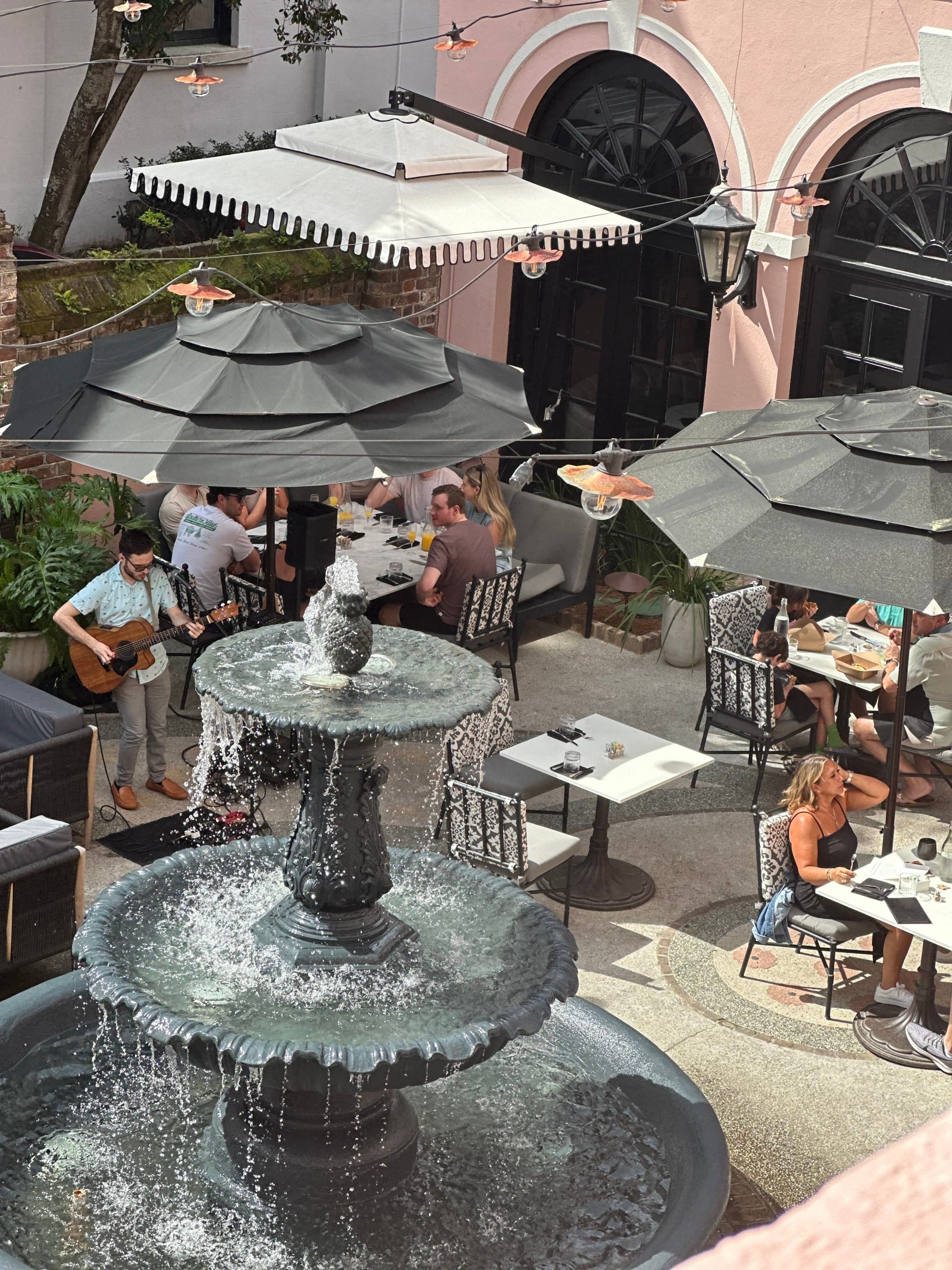 A view of a fountain and people dining on a patio with a person playing live music.