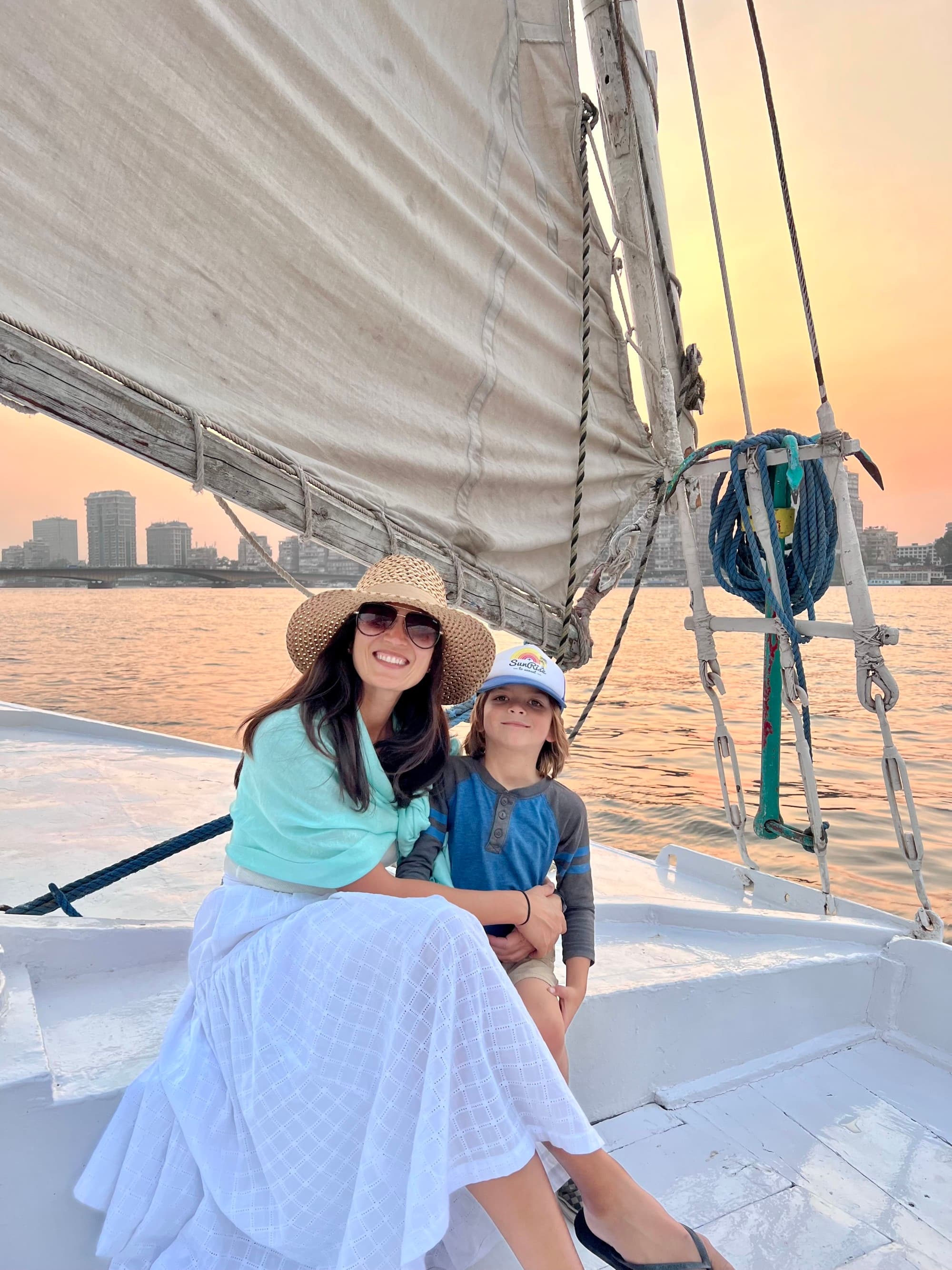 a woman in a sunhat and sunglasses sits on a sailboat with her young daughter