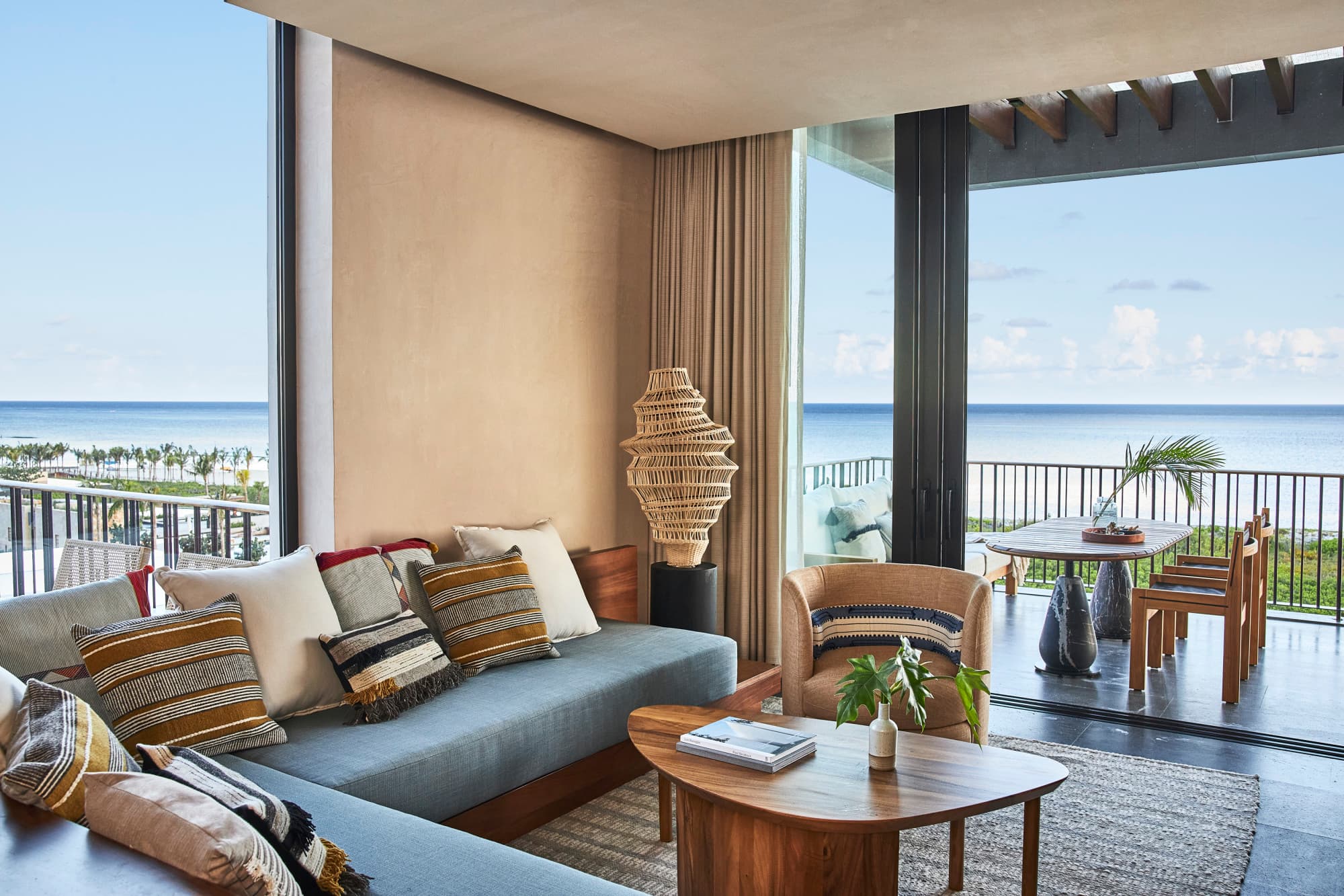 a blue L-shaped couch with patterned pillows sits in an open-air living room with a modern straw light fixture