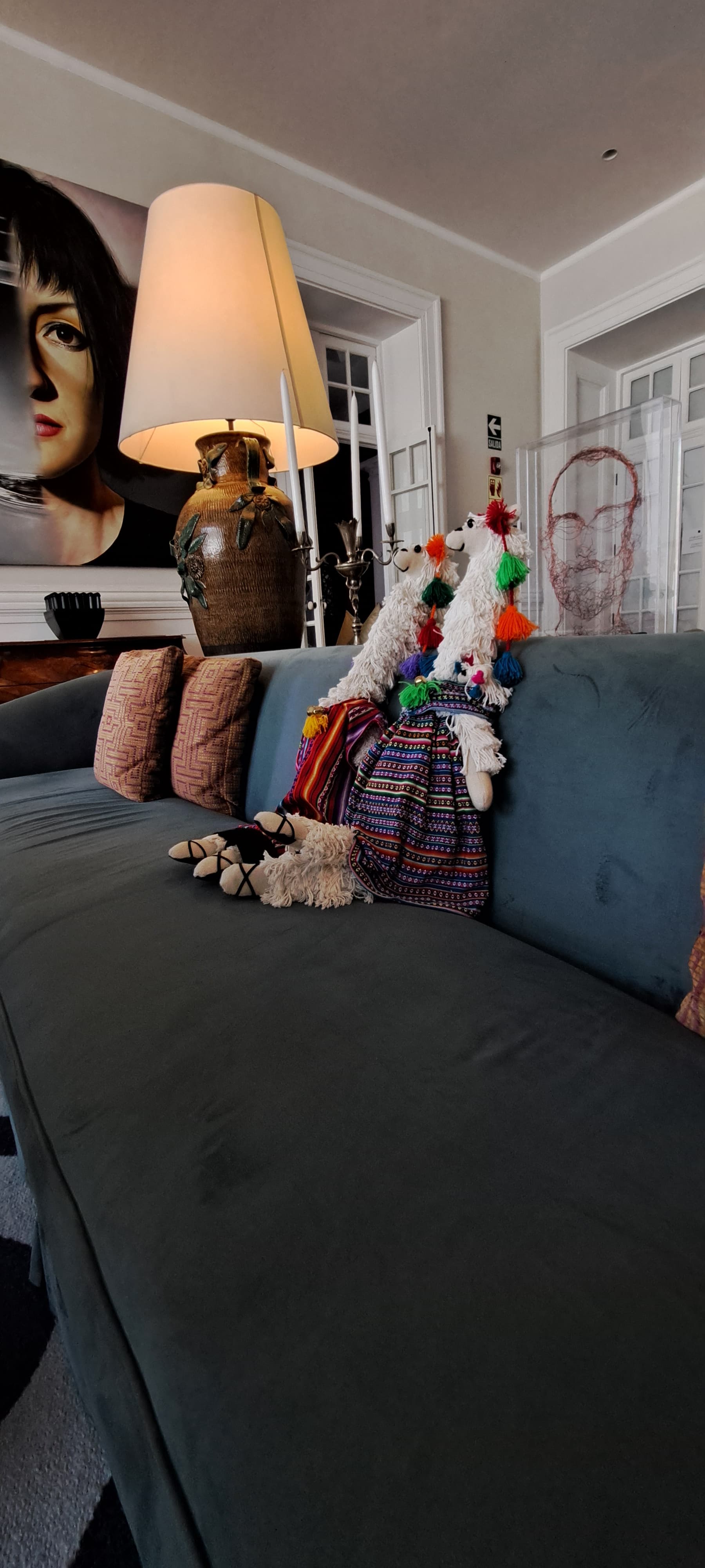 A sofa with decorative pillows, a lamp and a piece of artwork showcasing someones face hanging up on the wall.