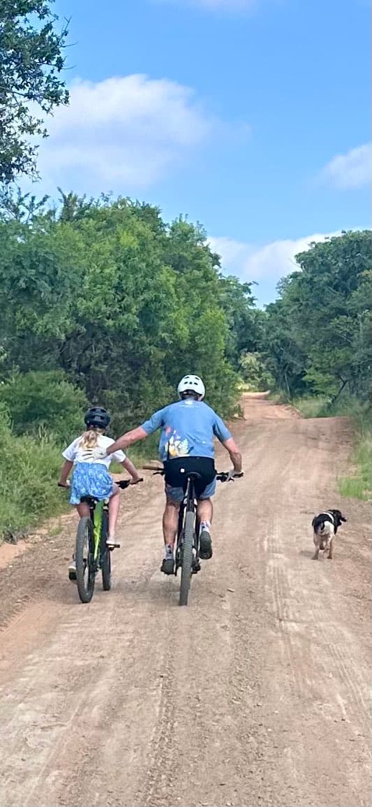 A dirt bike trail with two people and an animal traveling forward. They are also surrounded by trees on each side.