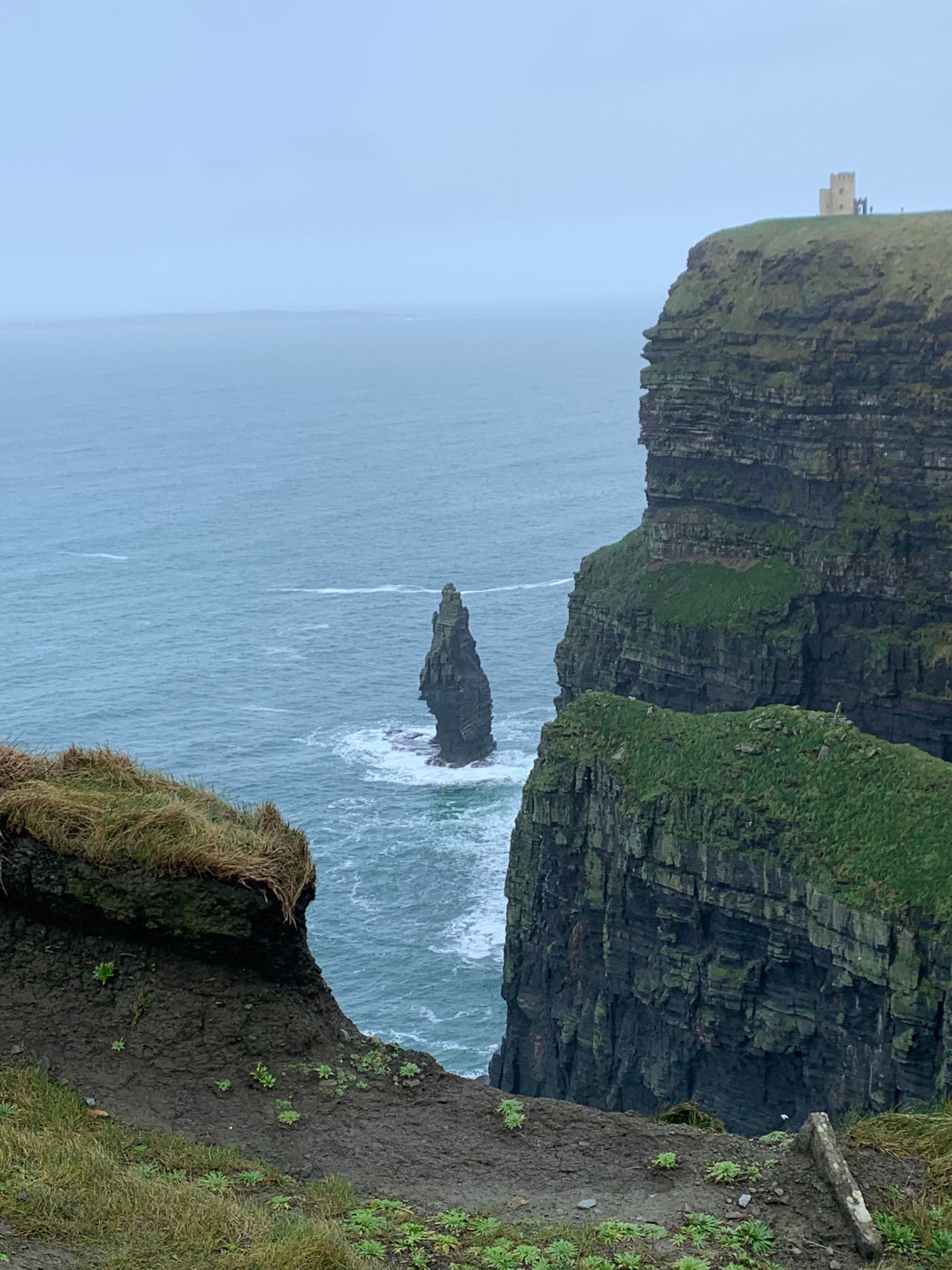 A view of green and rocky cliffs with the water in the background on a cloudy day.