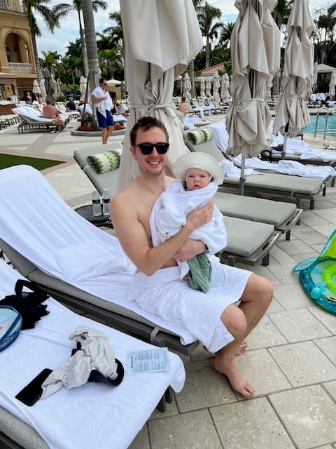 A person holding a baby wrapped in a towel while sitting on an outdoor lounge chair