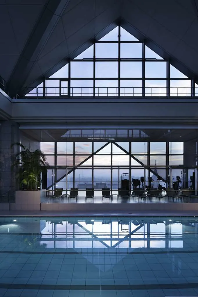 a pool in an atrium with glass ceilings and a large window overlooking a city