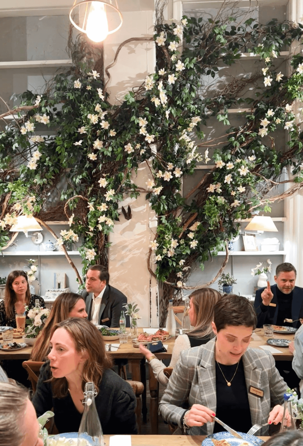 people sit at a wooden table and eat in front of a wall covered with decorative vines
