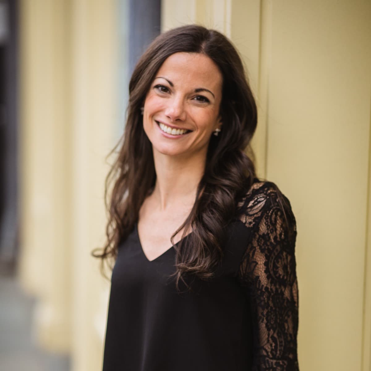 a beautiful woman with a black shirt and long brown hair smiles outside