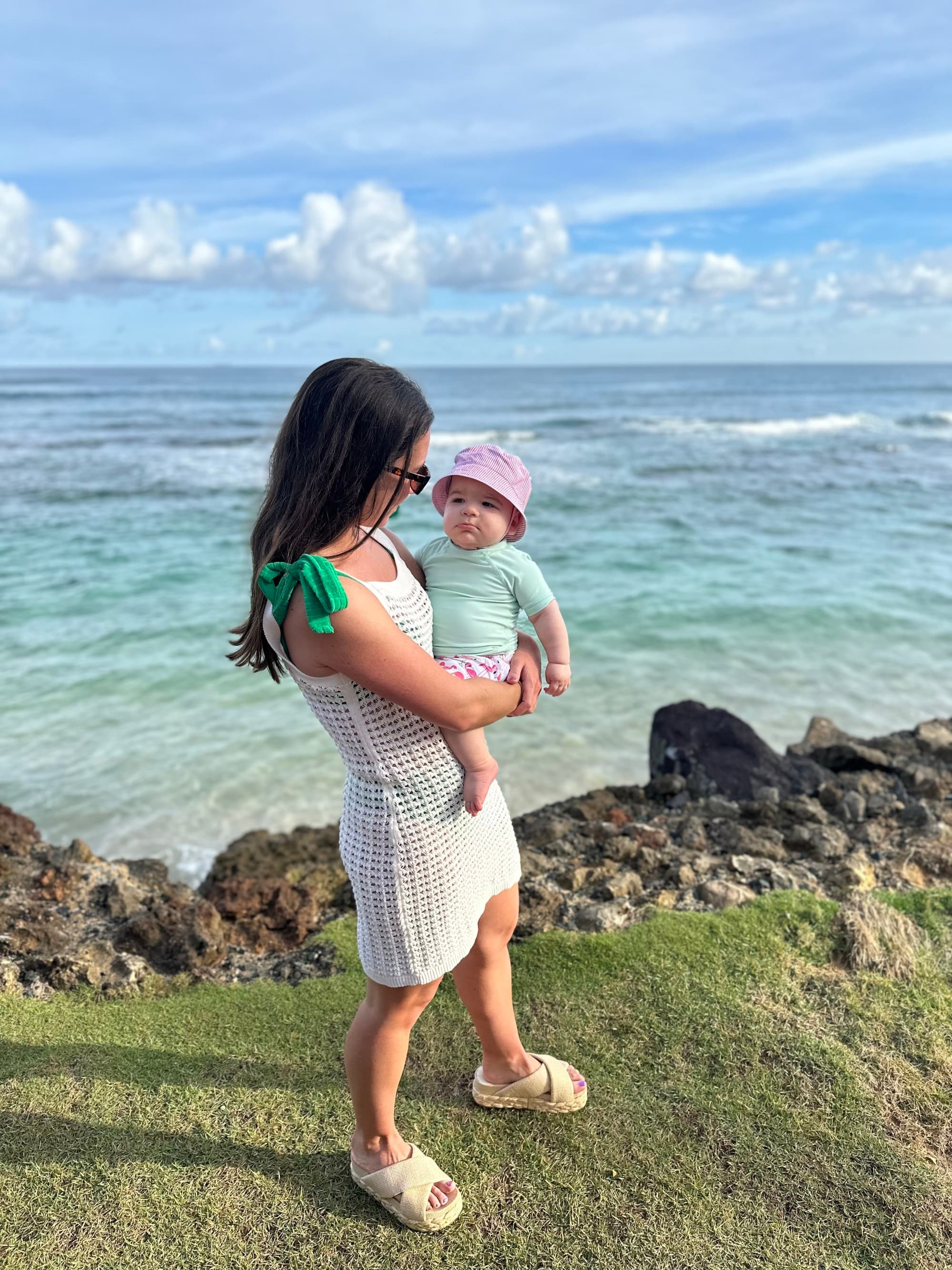 a woman in a white dress holds a baby near the sea