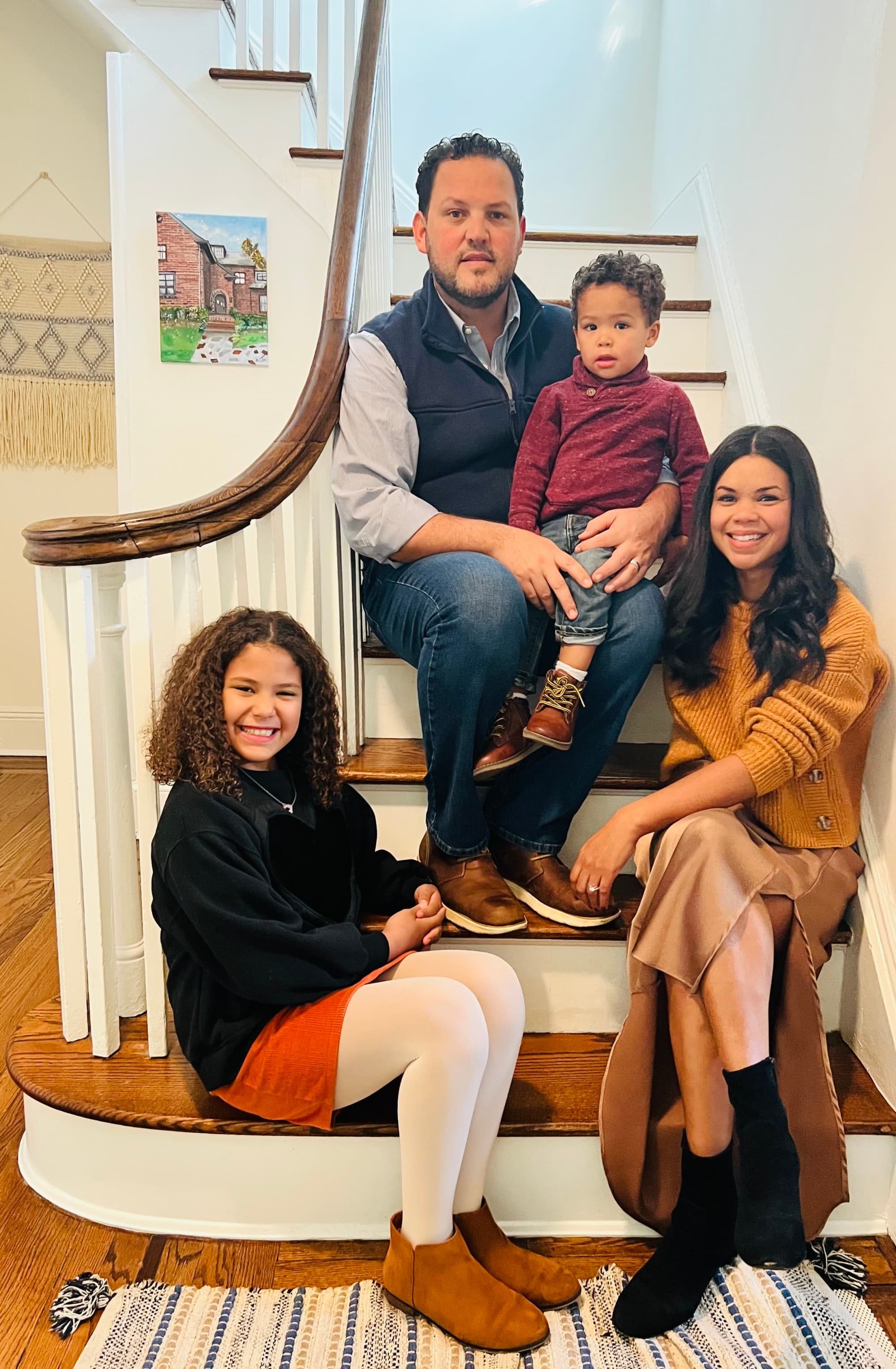 A mother and father sit on a staircase with their two children