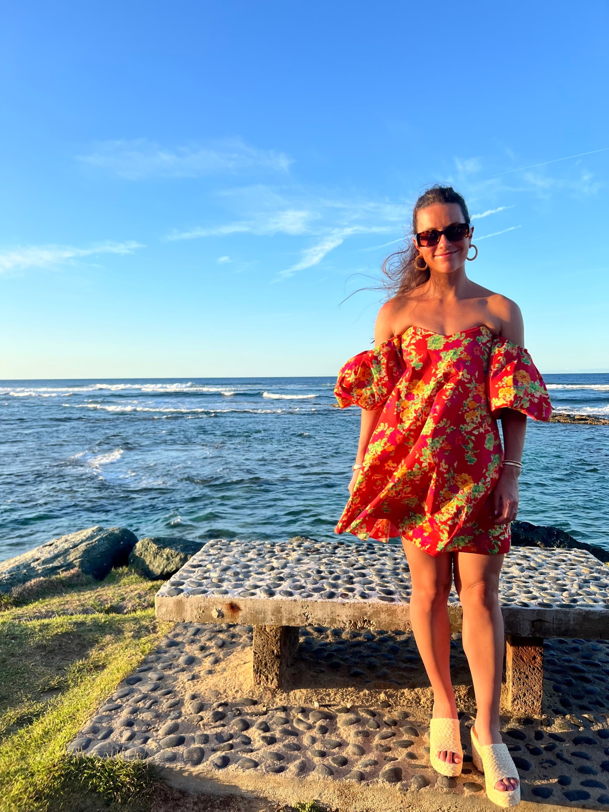 a woman in a flower-patterned dress stands near the ocean