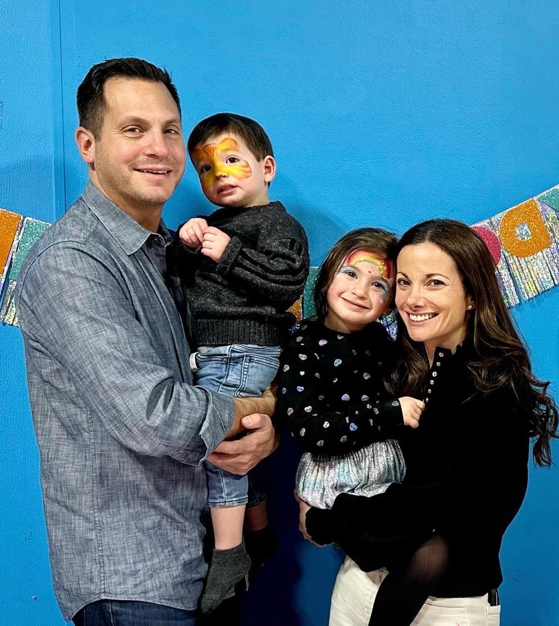a man and a woman hold two children who have colorful face paint