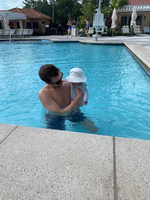 A person holding a baby while in an outdoor pool