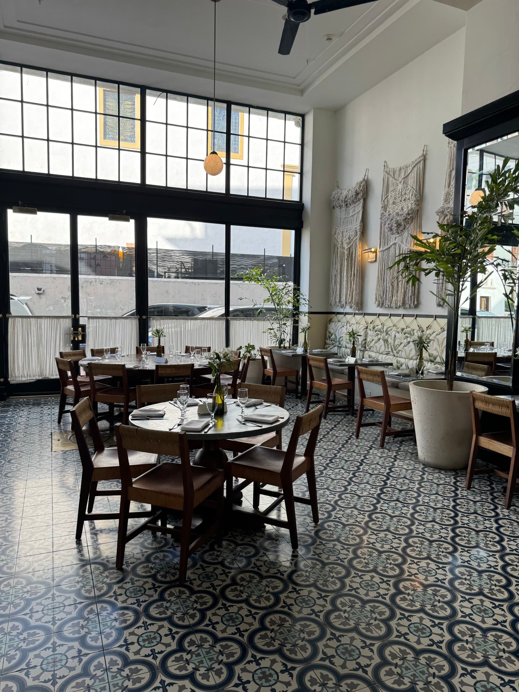 Dining area with a mosaic tile floor, large windows and plants.