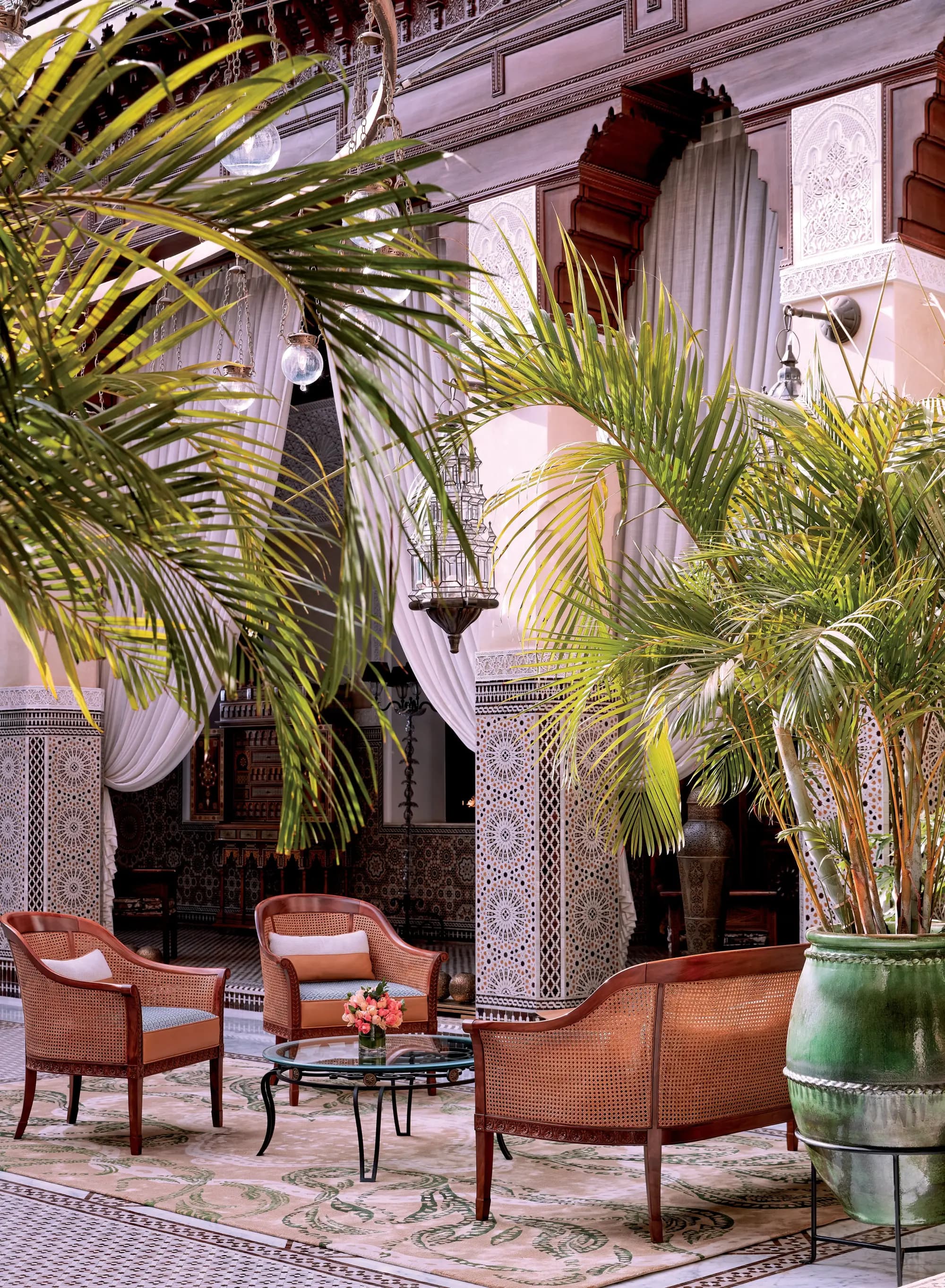 a couch and two chairs in an opulent courtyard filled with plants, curved arches, and intricate tile work