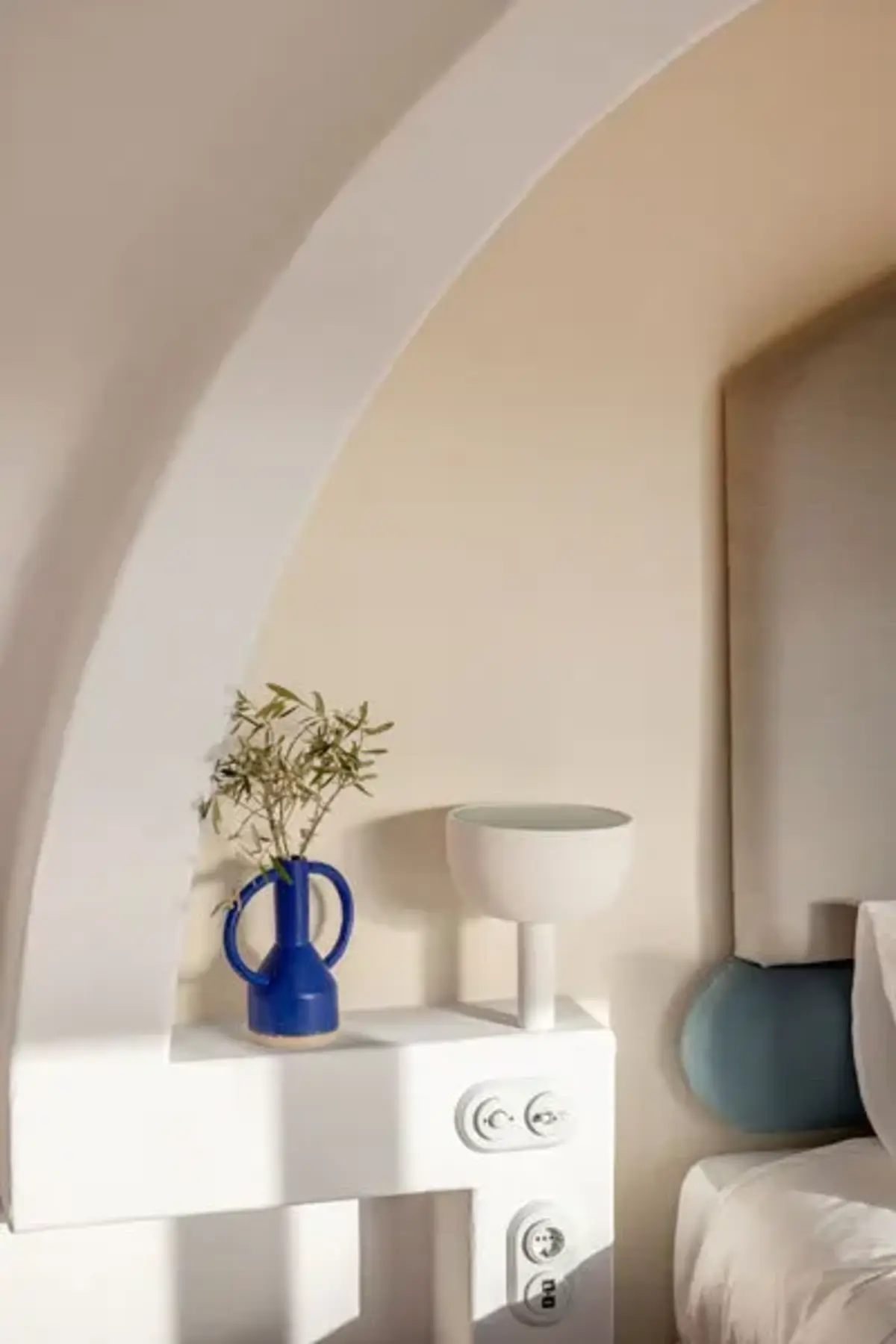 a modern blue vase holding flowers on a white bedside table