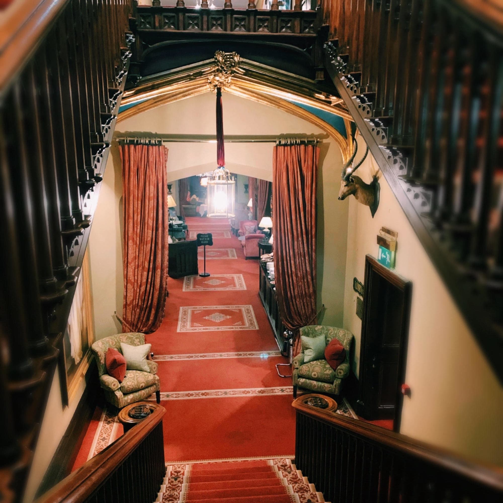 A view of stairs leading downward to luxurious red carpeting, curtains and lavish woodwork.