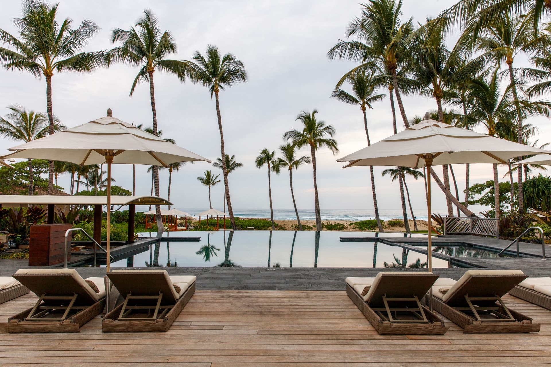 two lounge chairs on a wooden deck overlooking an oceanfront pool