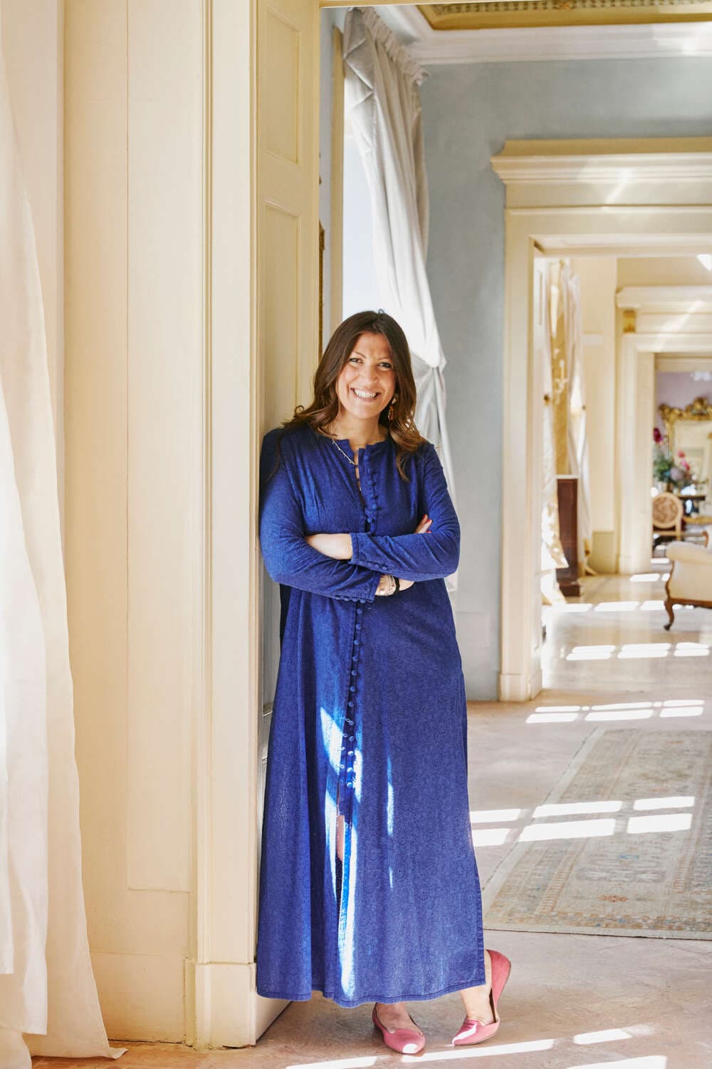 a woman in a long blue dress leans against a white wall