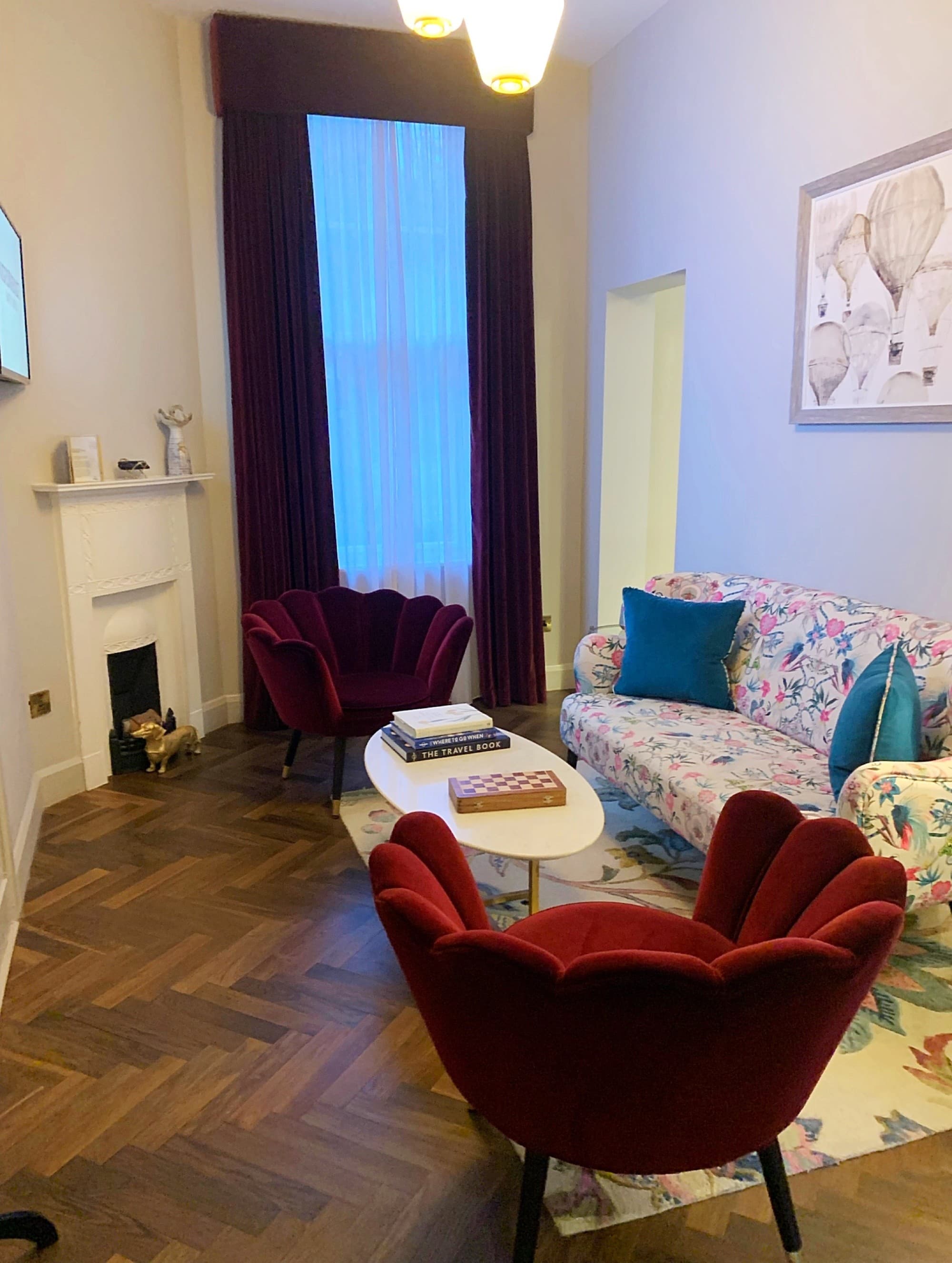 A seating area in a hotel room with two red chairs and a floral patterned couch