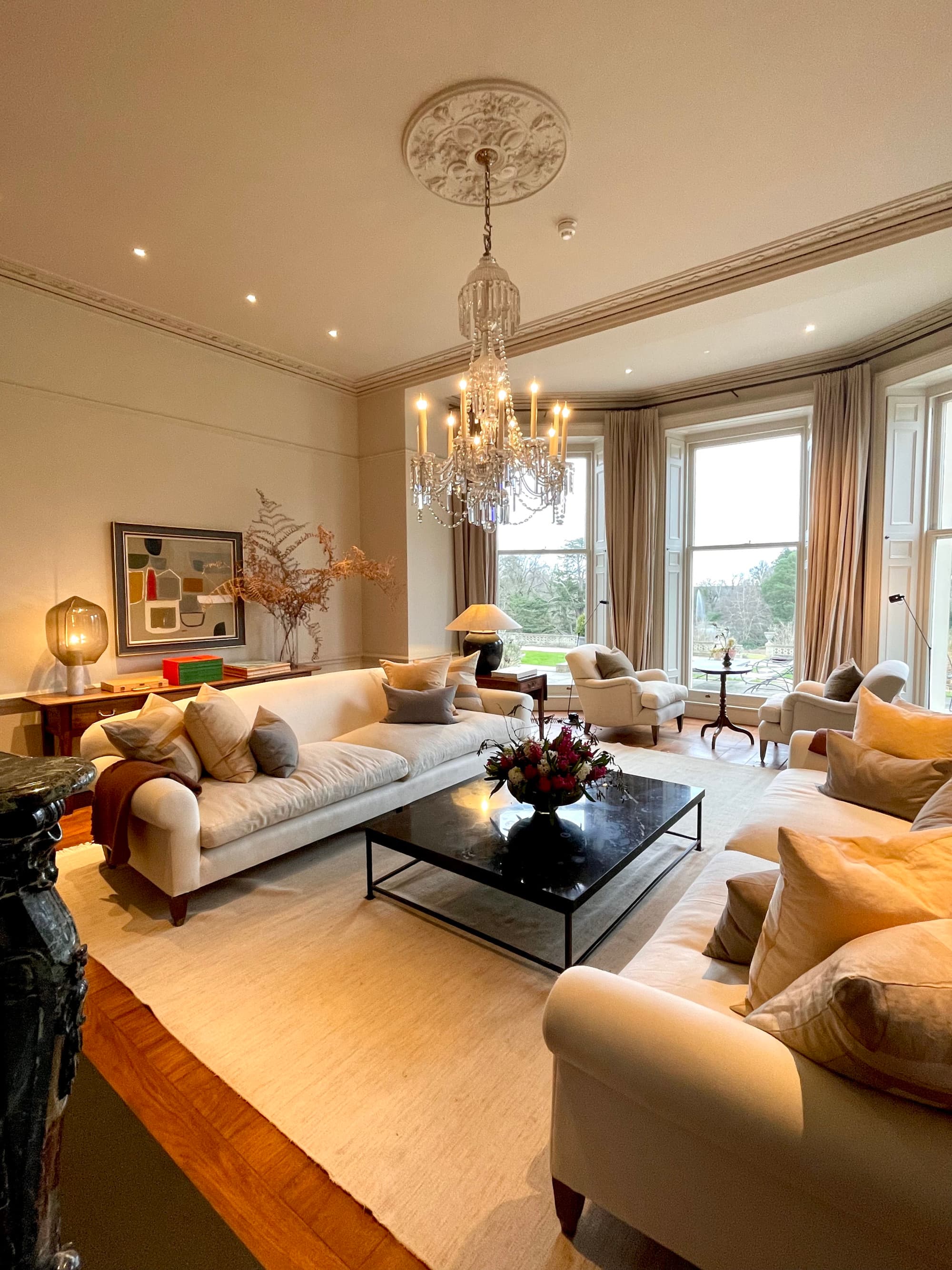 A large guest room with couches, windows overlooking a field and a chandelier