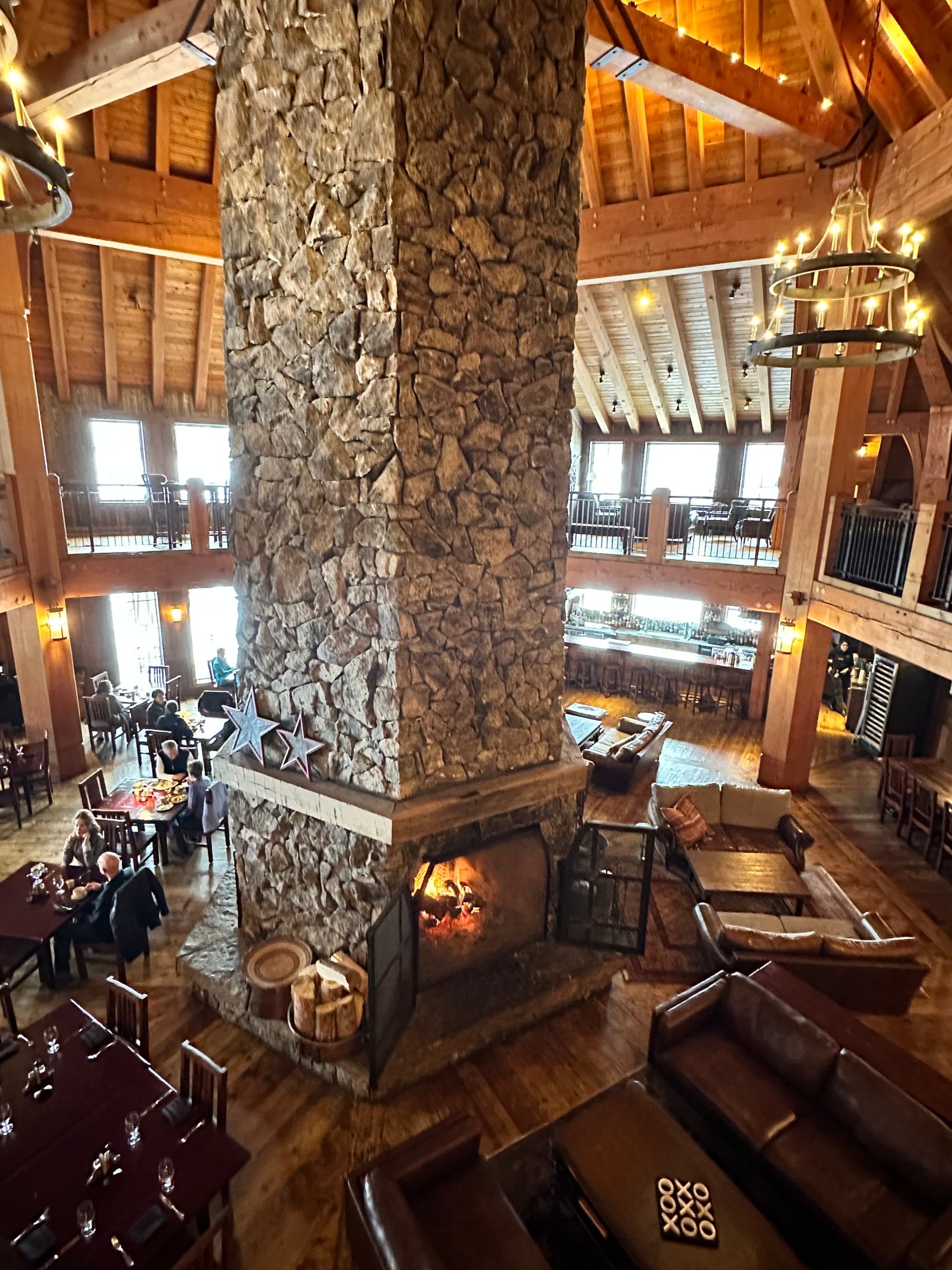 An aerial view of a hotel lobby with a large stone fireplace in the center surrounded by large chandeliers, wood paneled ceilings, and seating areas.