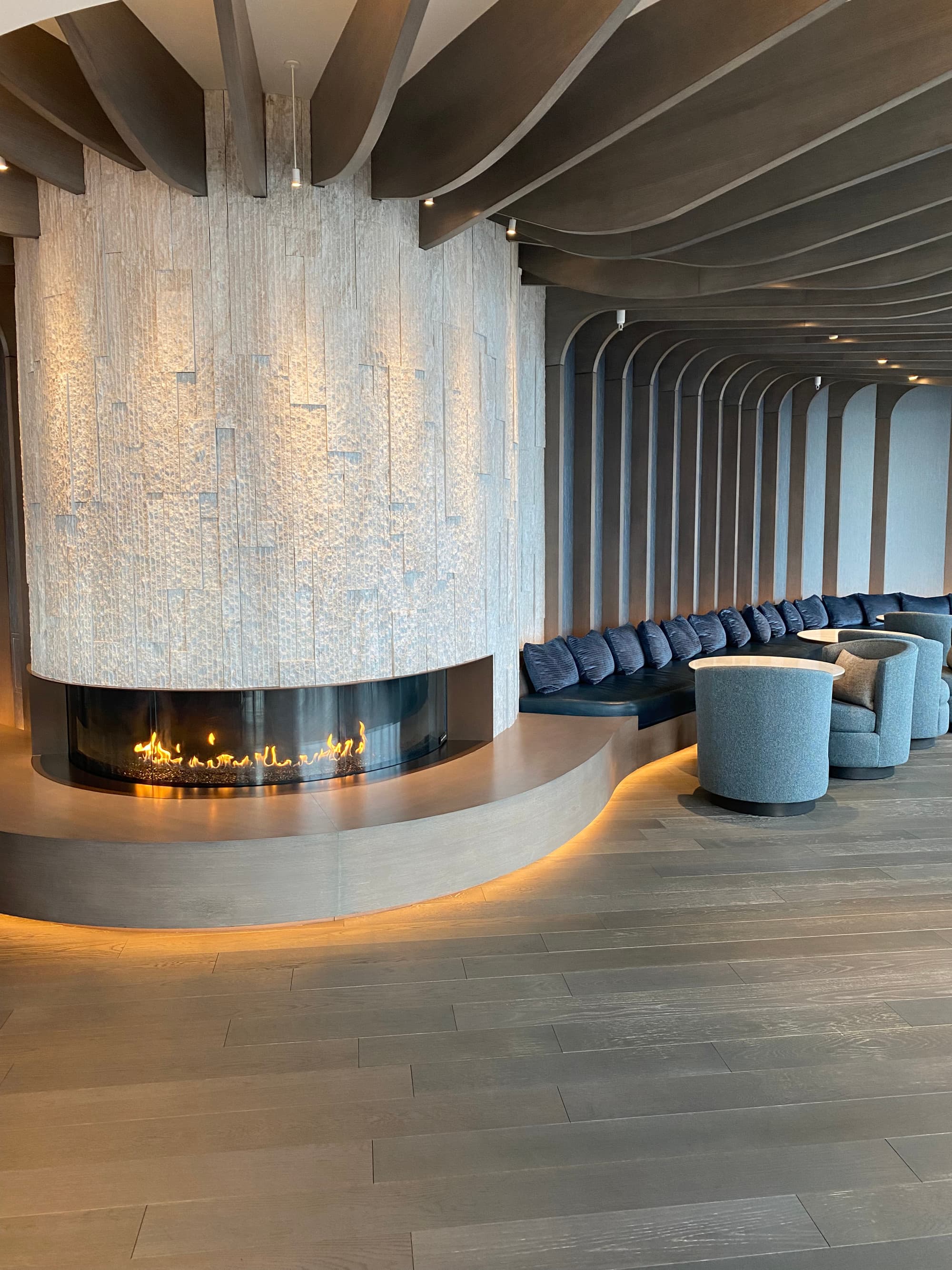 A beautiful room with wood paneled ceilings, a curved modern-style fireplace and lounge seating on the right.