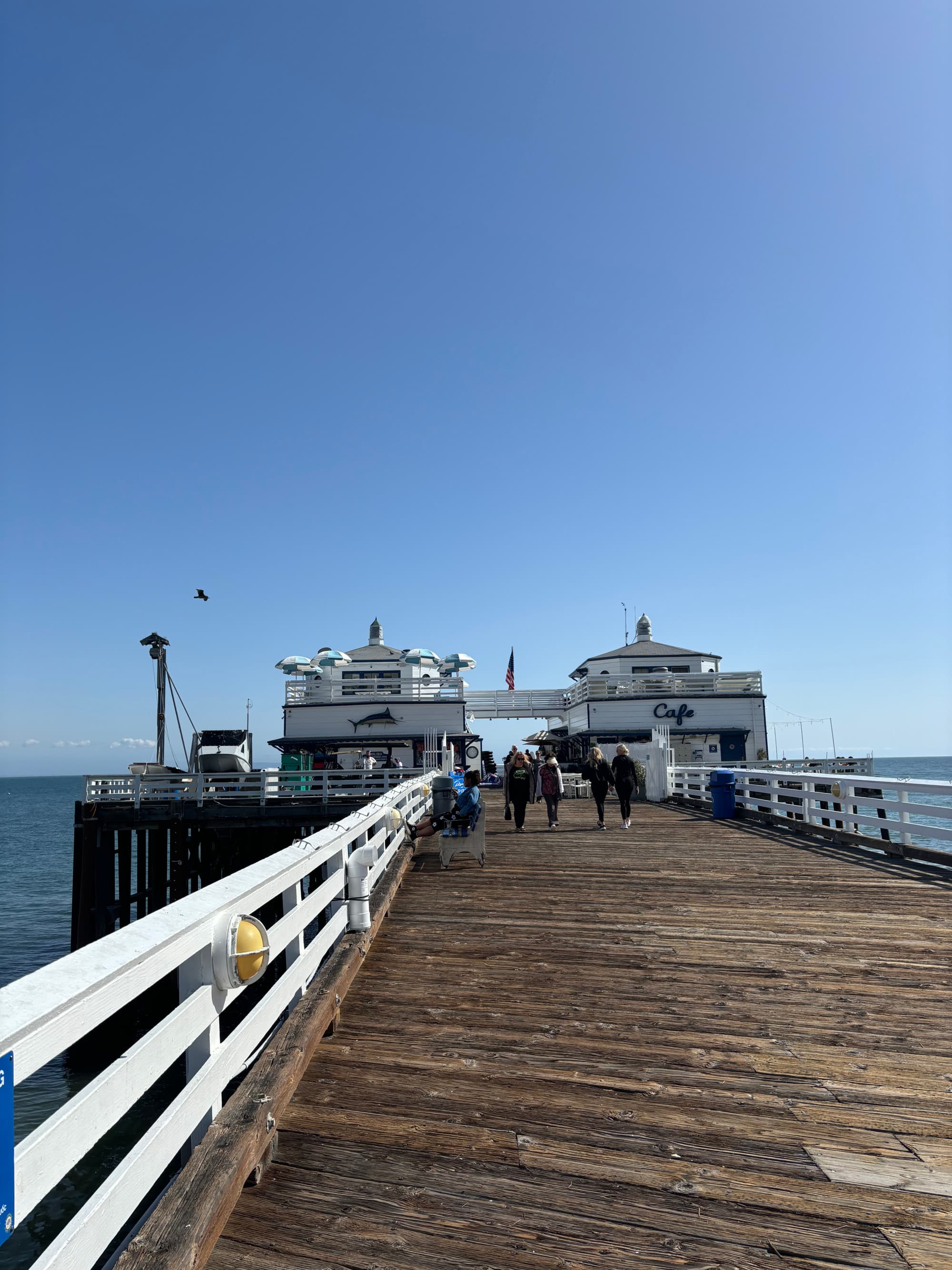 A view of the wooden boardwalk at the Malibu pier with people walking in the distance and lookout points.