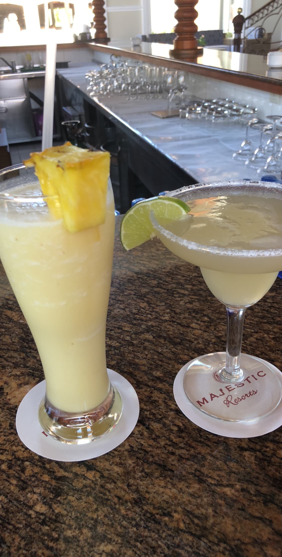 Two tropical drinks with fruit wedges on the rim of each glass at a bar.