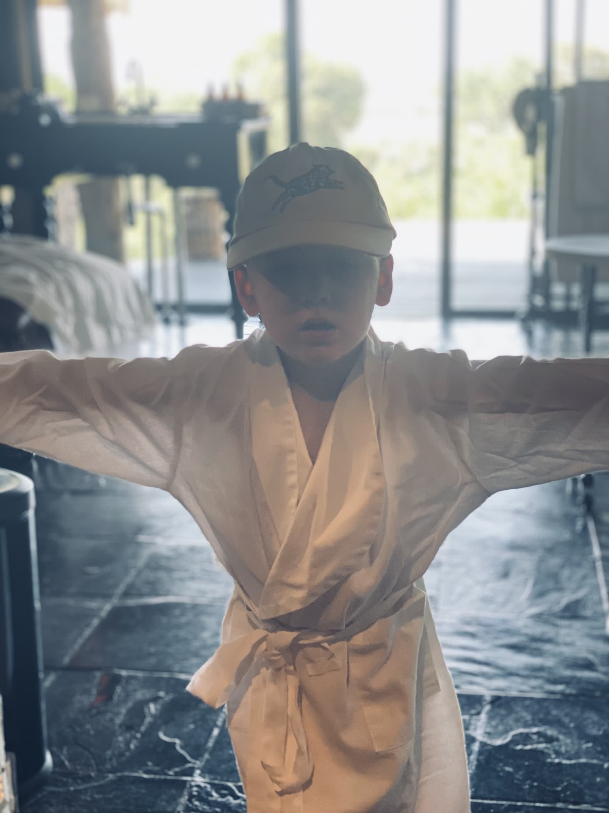 Child posing in a white robe with a cap inside a hotel room