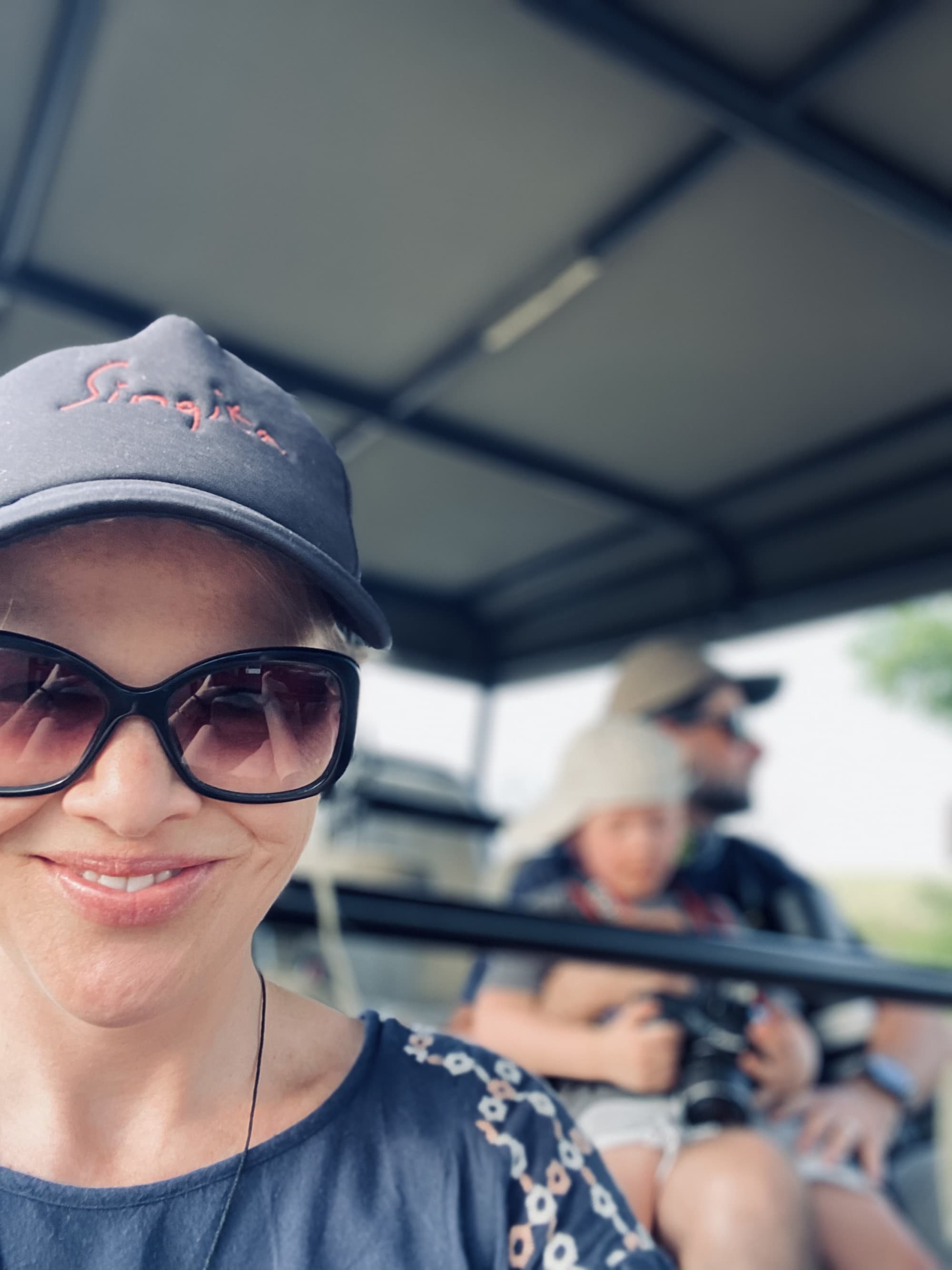 Travel advisor Sharon posing in a cap and sunglasses on safari vehicle with husband and child behind