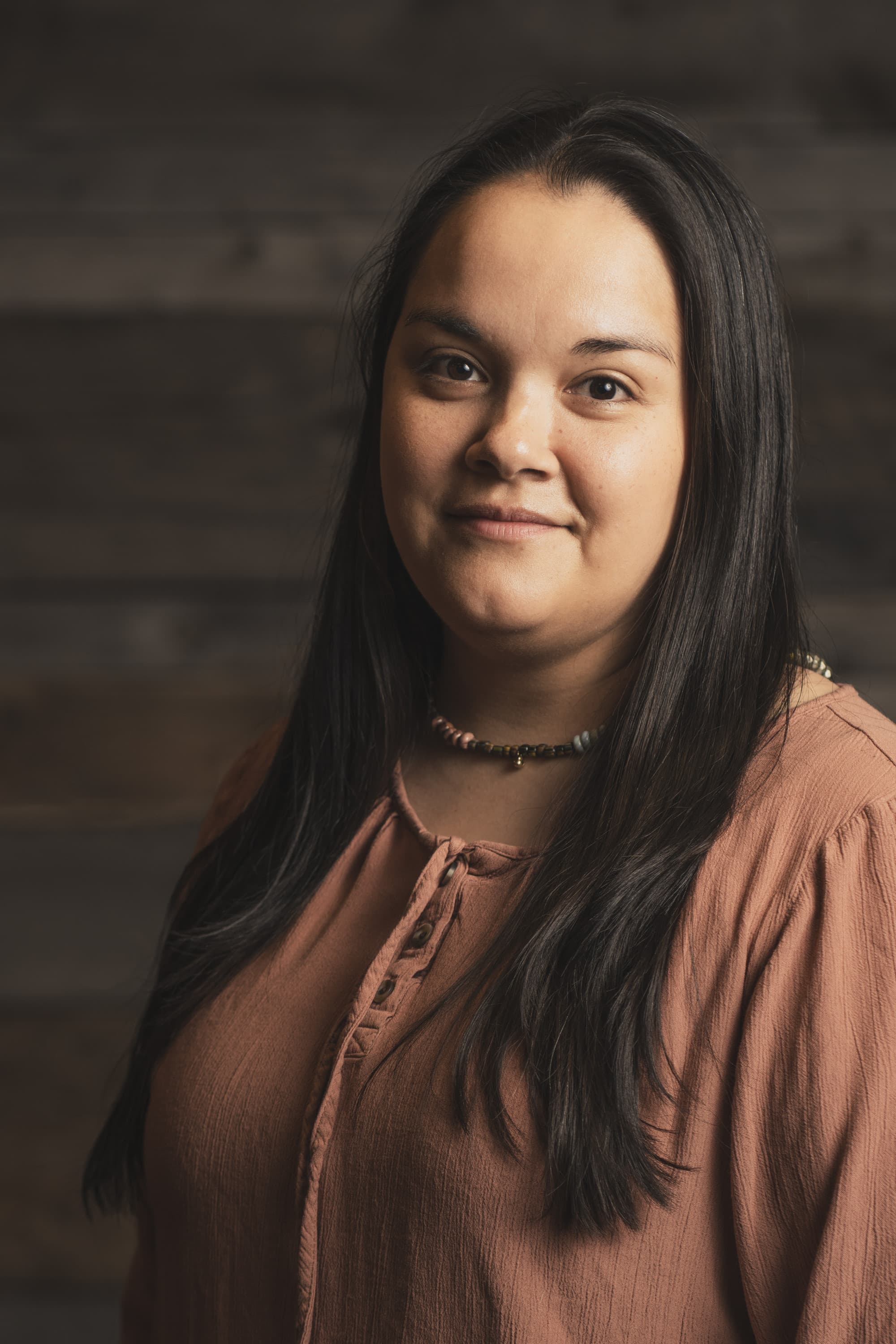 a woman with long black hair wears a pink shirt and smiles