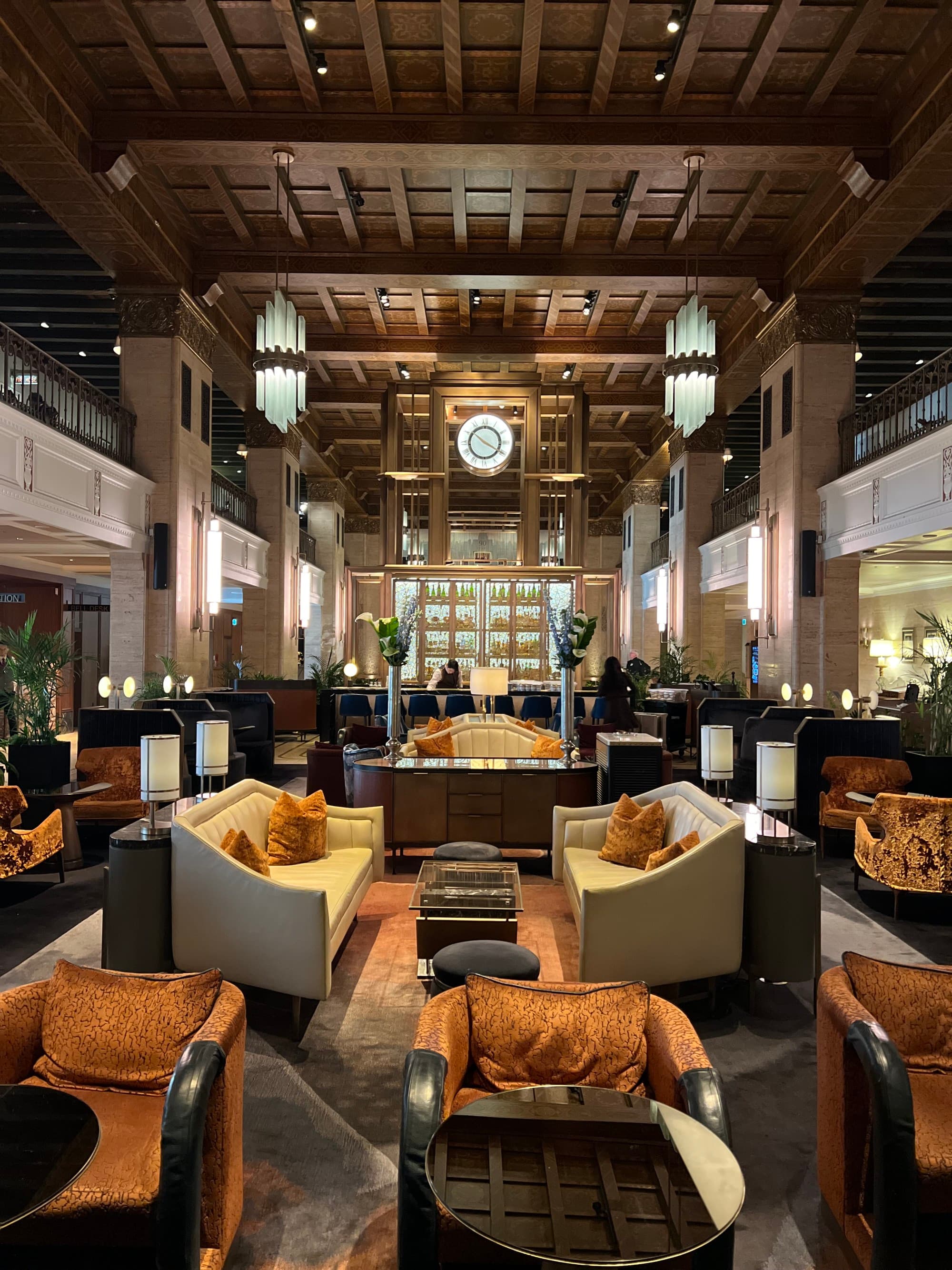 A view of a lounge area at the hotel with cream sofas, orange cushions, wood paneled ceiling and an elegant bar at the far end