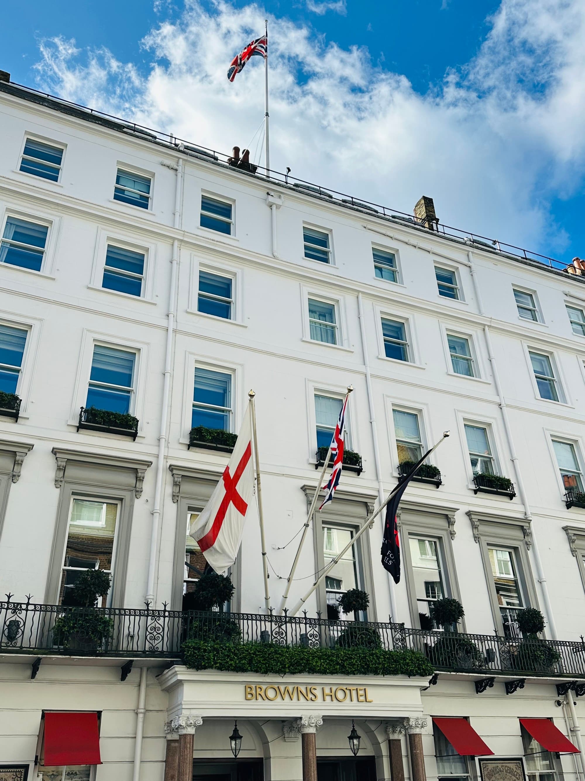 The exterior of Brown's Hotel, an elegant whyite building with many windows and England flags flying above the entrance