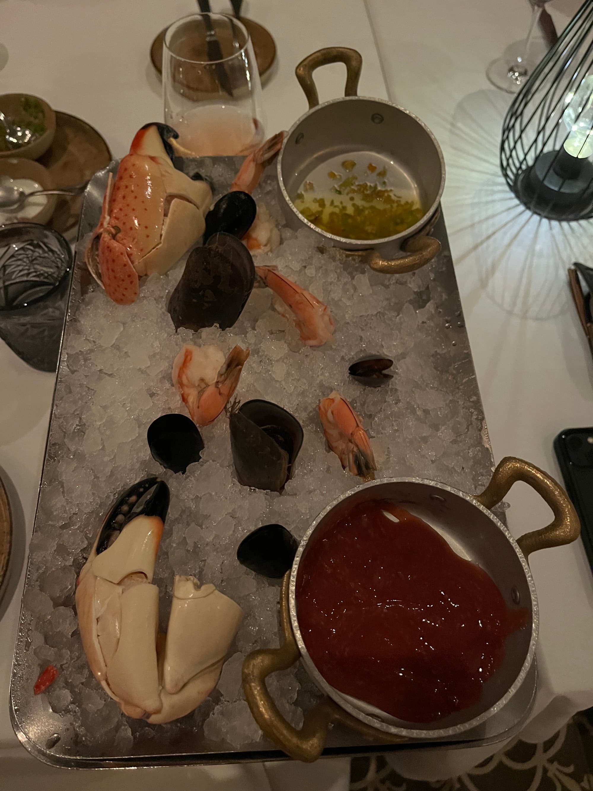 A view of fresh seafood over ice, with two containers of sauce on the right side of the tray.