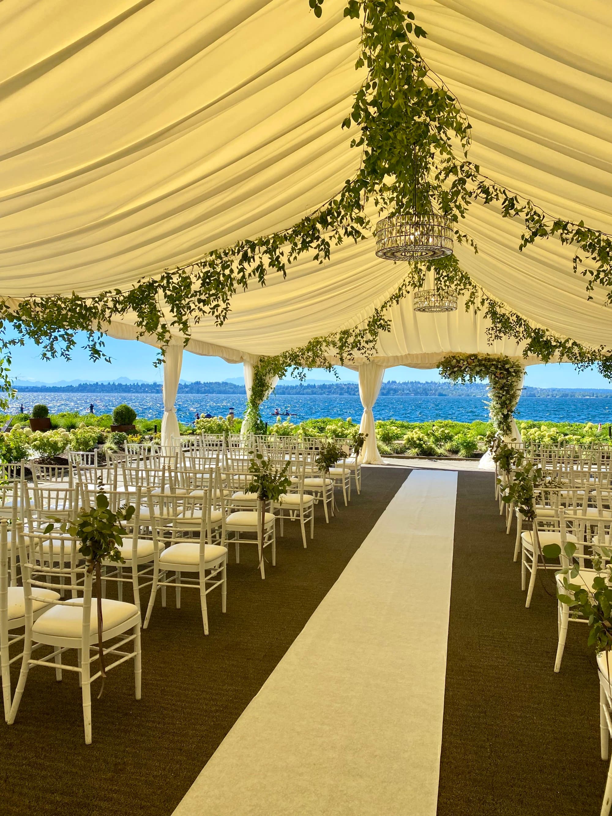 A wedding venue with a white walkway, white chairs, a white canopy and vine detailing.