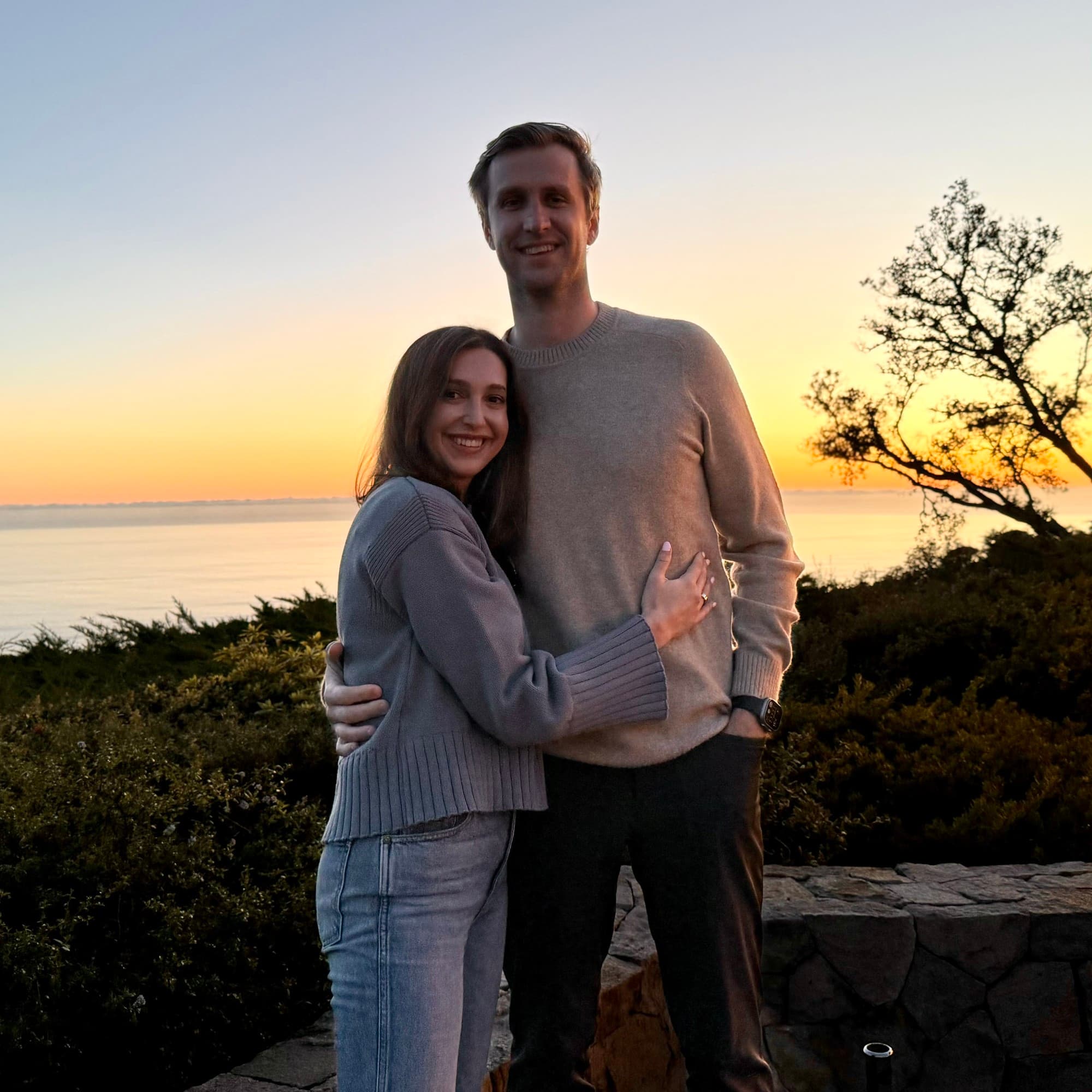A couple posing in front of a sunset and trees.