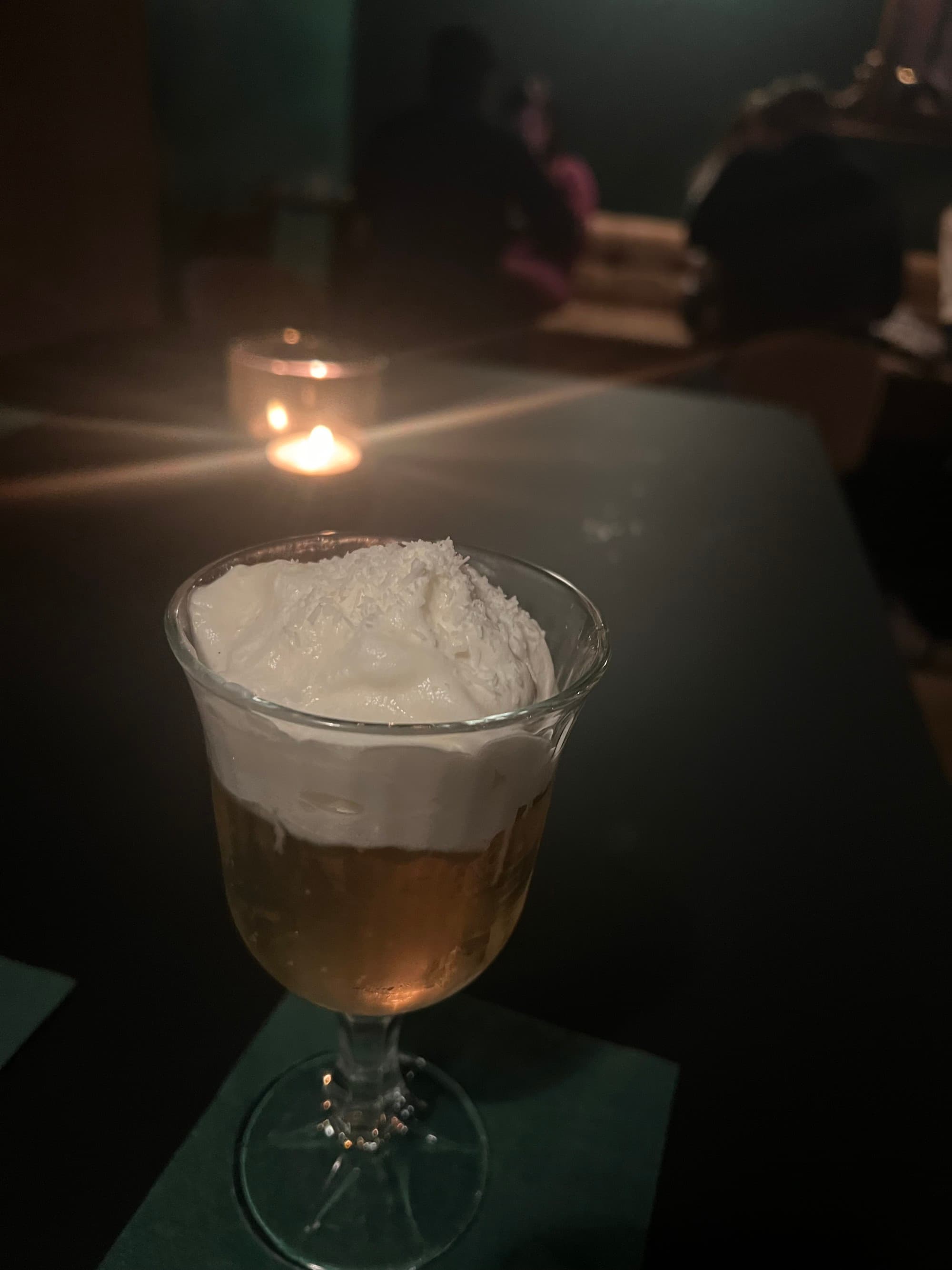 A cocktail with whipped cream inside of a dark bar, NeunDreivertel Bar