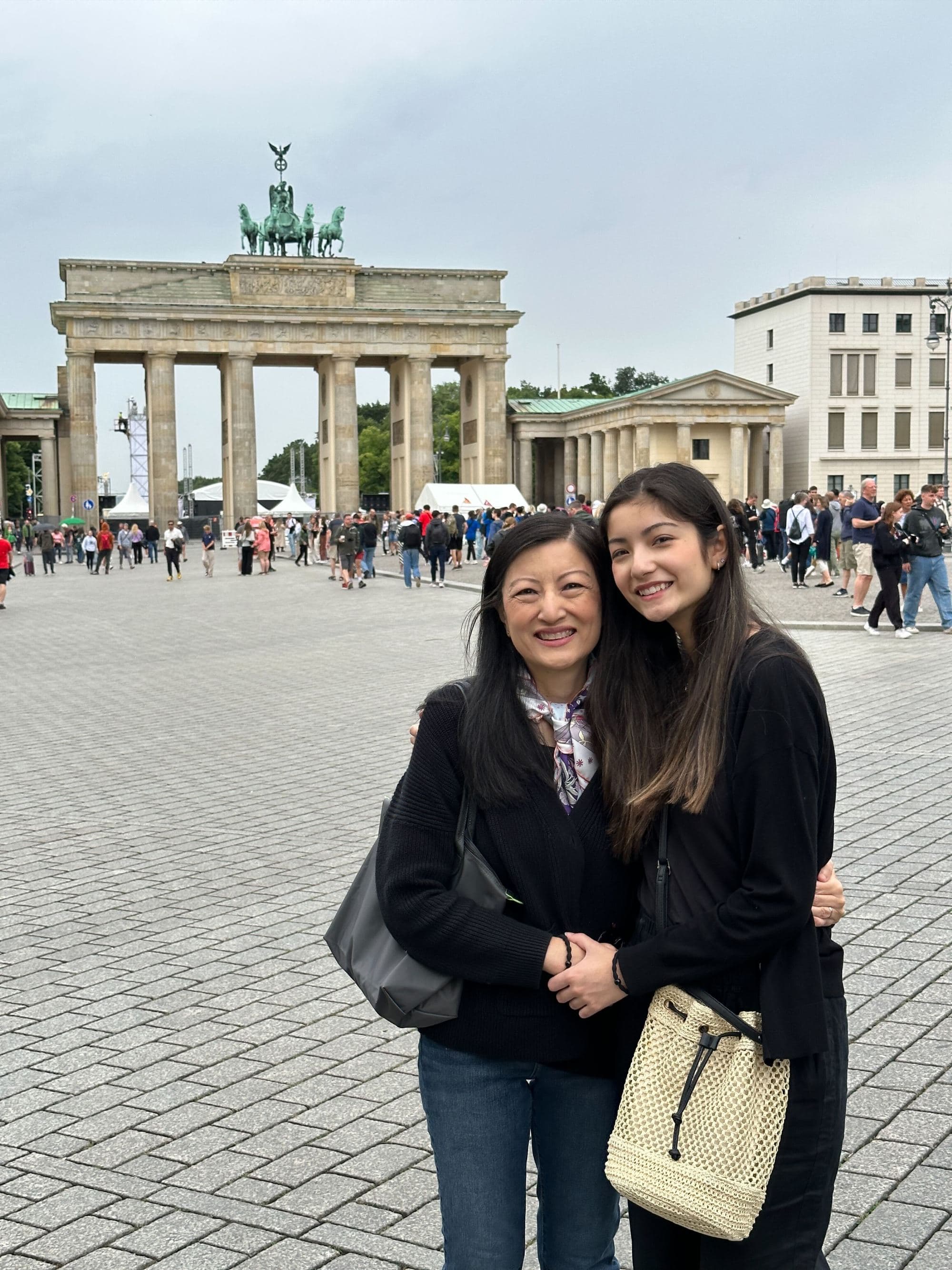 A mother and her daughter in black coats stand in an old town square