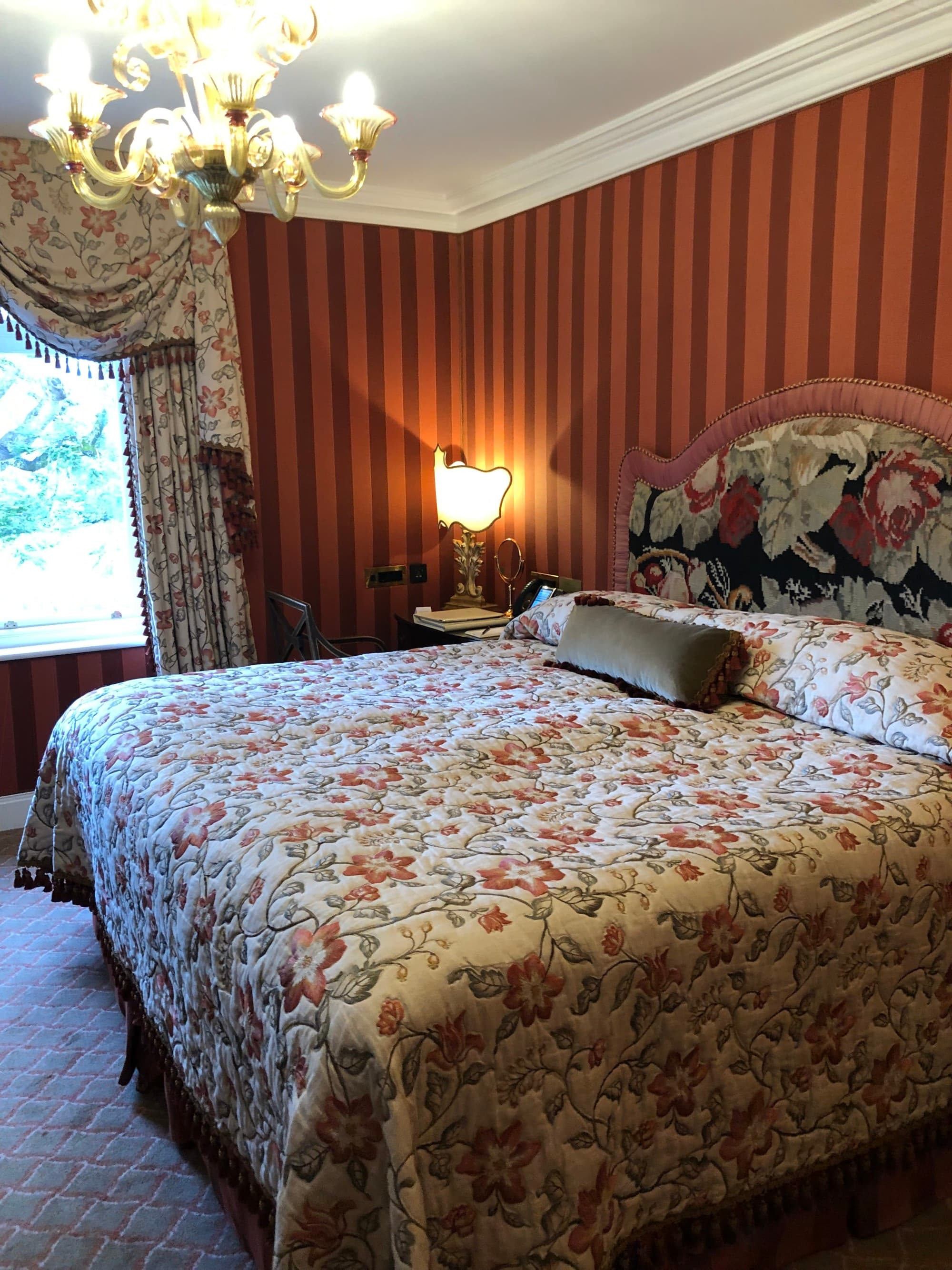 A hotel bedroom with a colorful bedspread and dark red walls and a chandelier