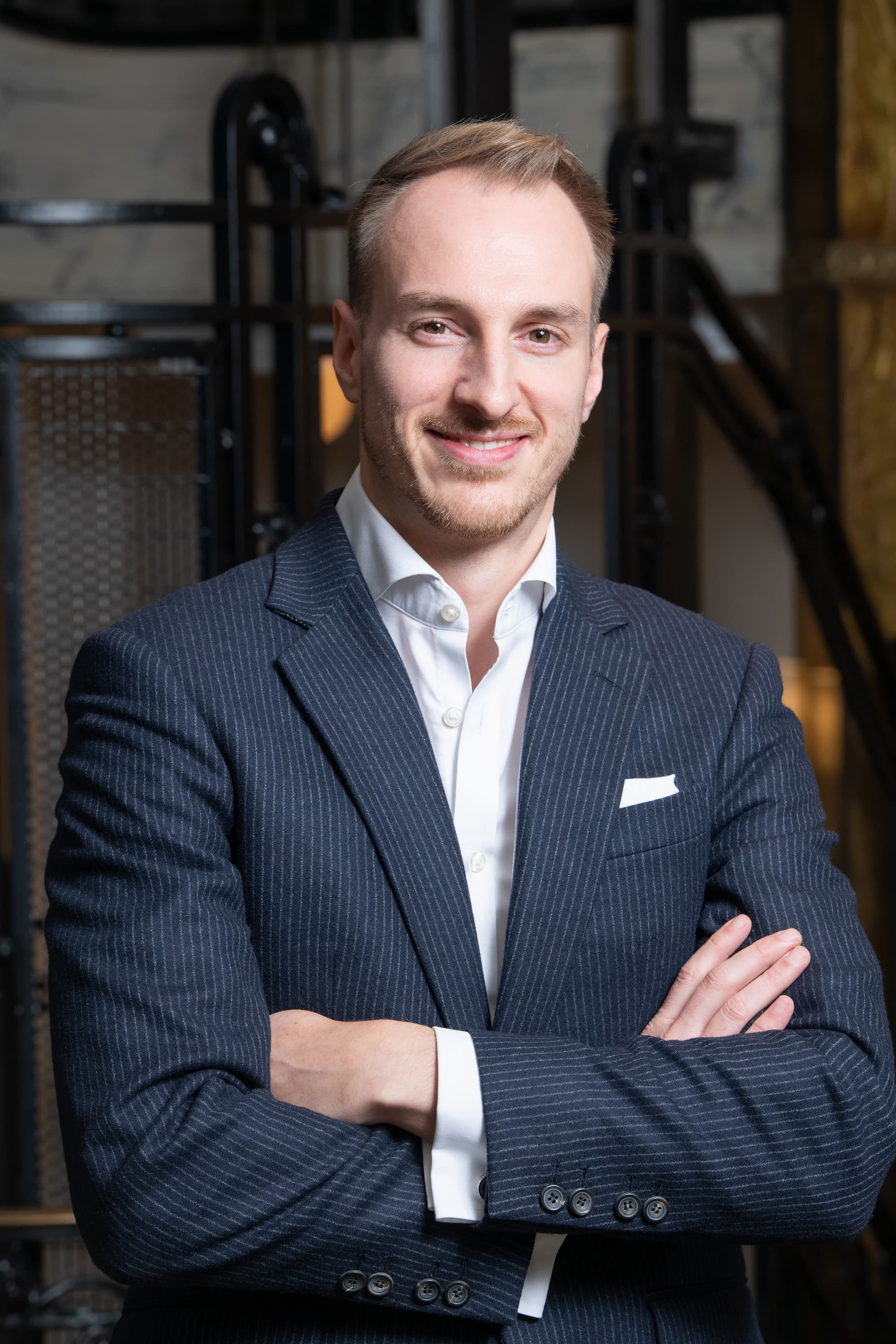 a man in a professional suit smiles and crosses his arms