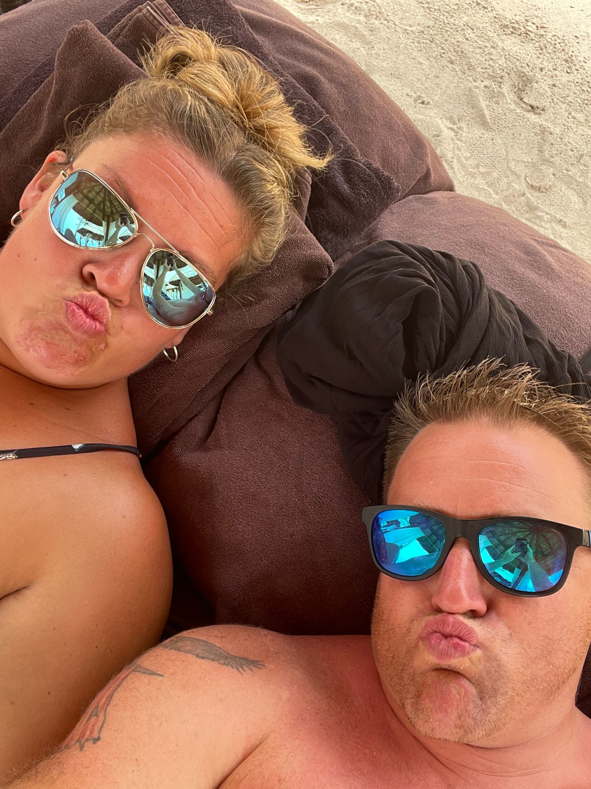 A couple laying on a beach lounger posing for a selfie photo
