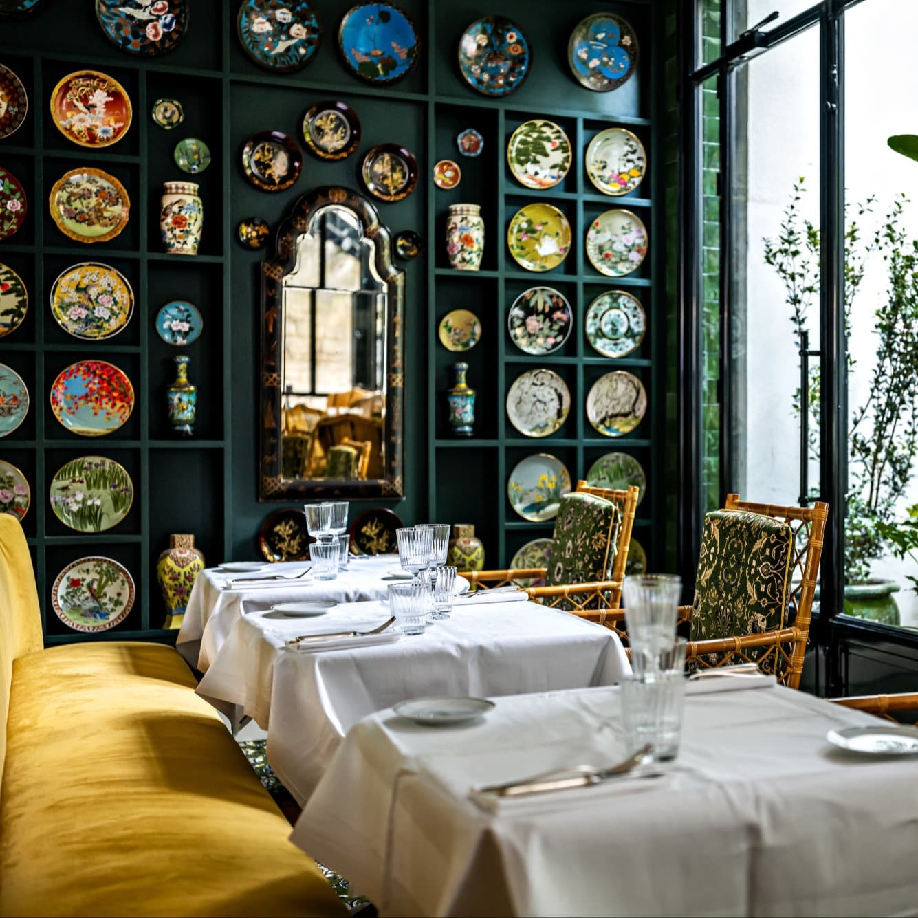 tablecloth-covered tables in a luxe dining room with a wall filled with decorative plates